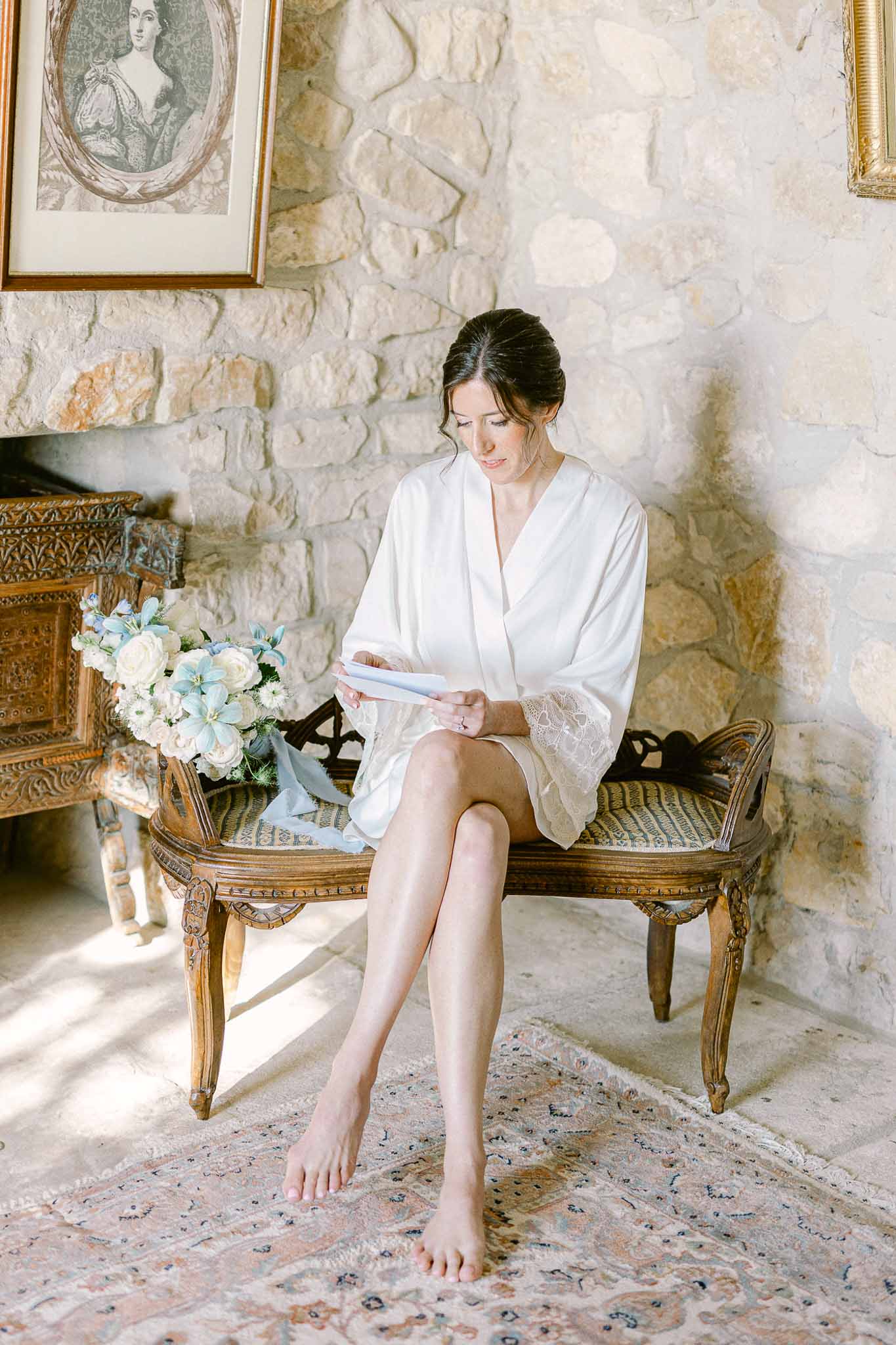 Bride in white silk robe holding bouquet and vows in ornate historic interior setting