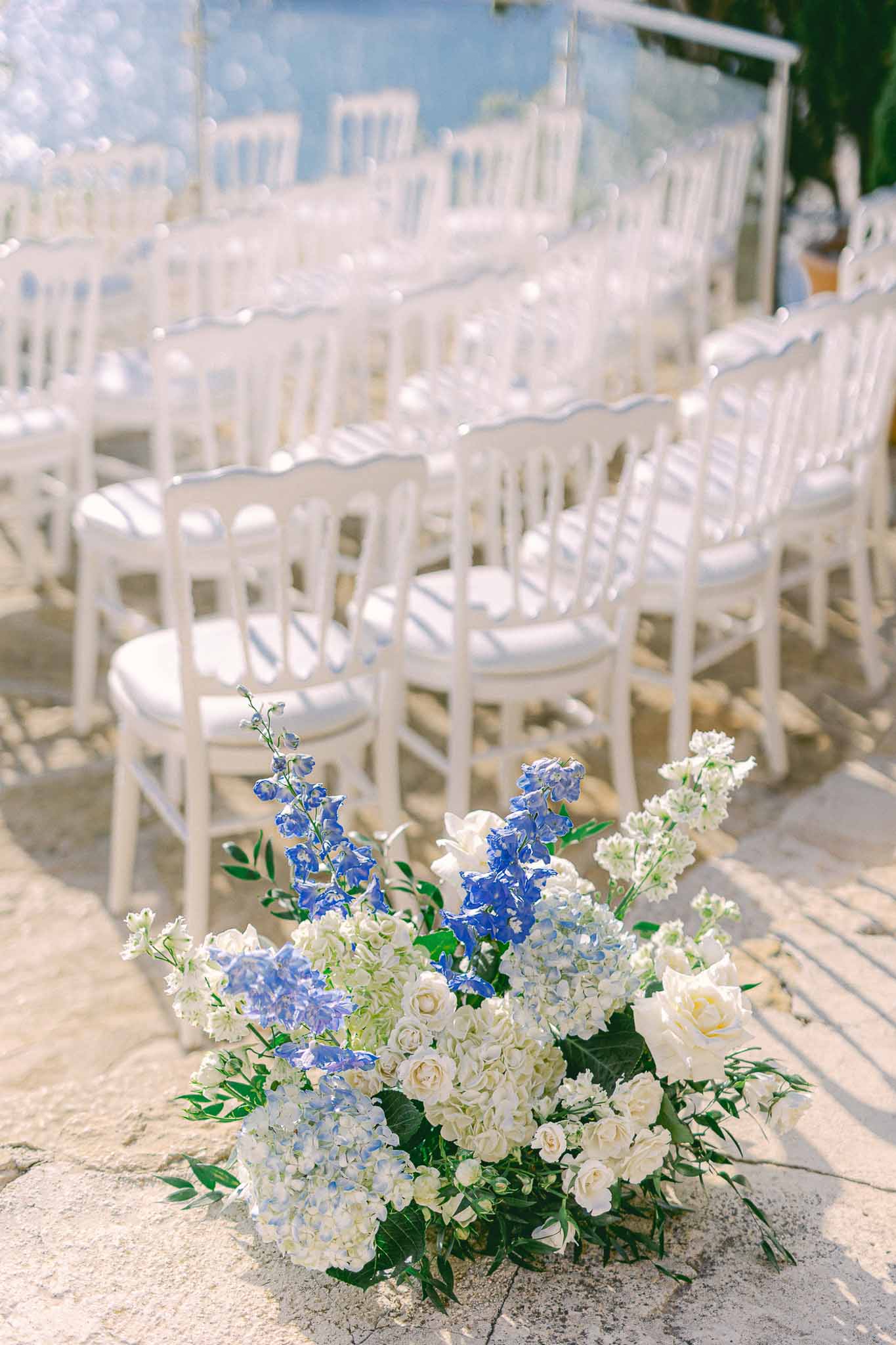 Ceremony aisle floral arrangement with white Chiavari chairs in outdoor garden wedding setup