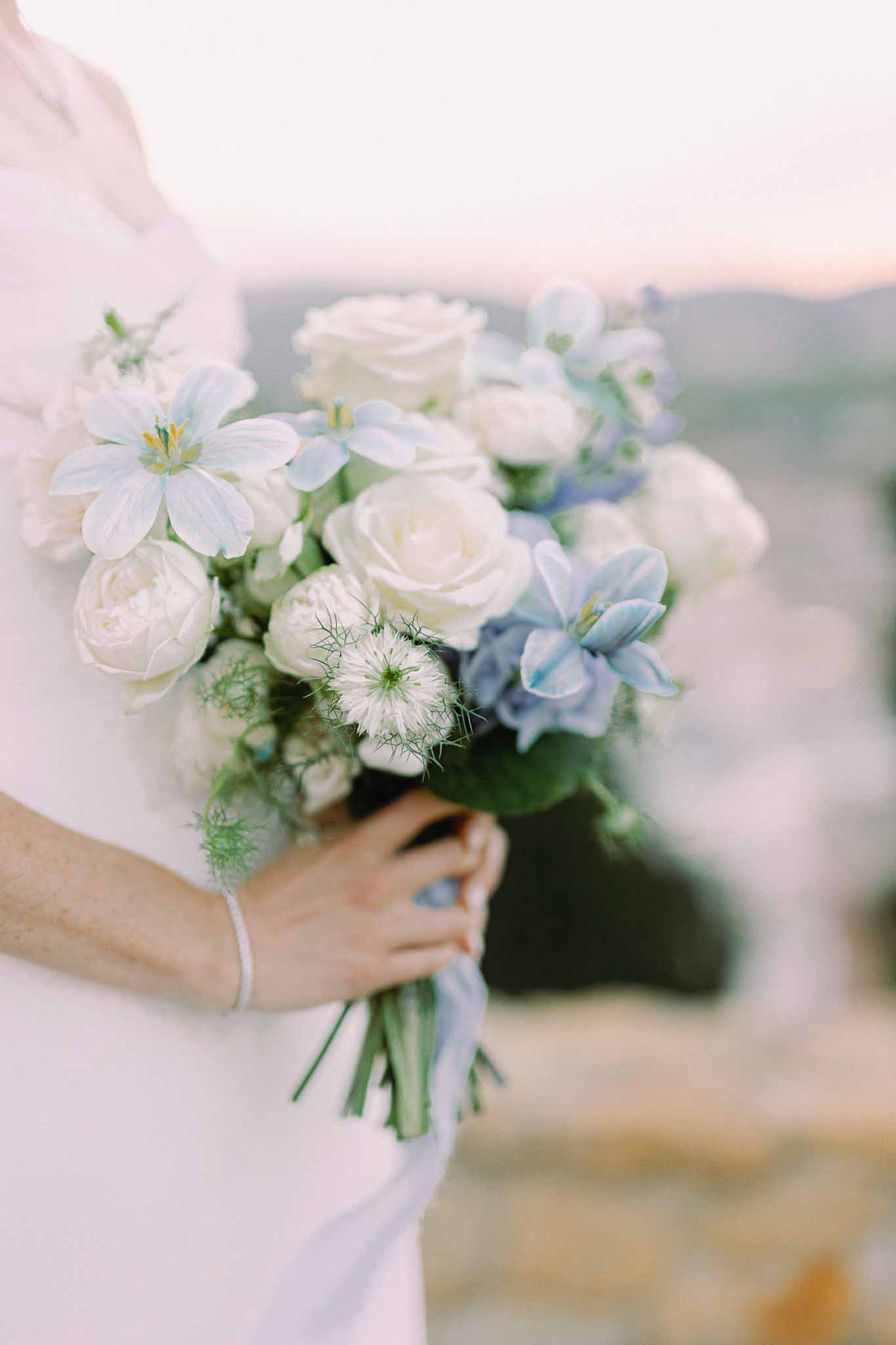 Bride holding white and blue bouquet with garden roses and delphinium at outdoor wedding venue