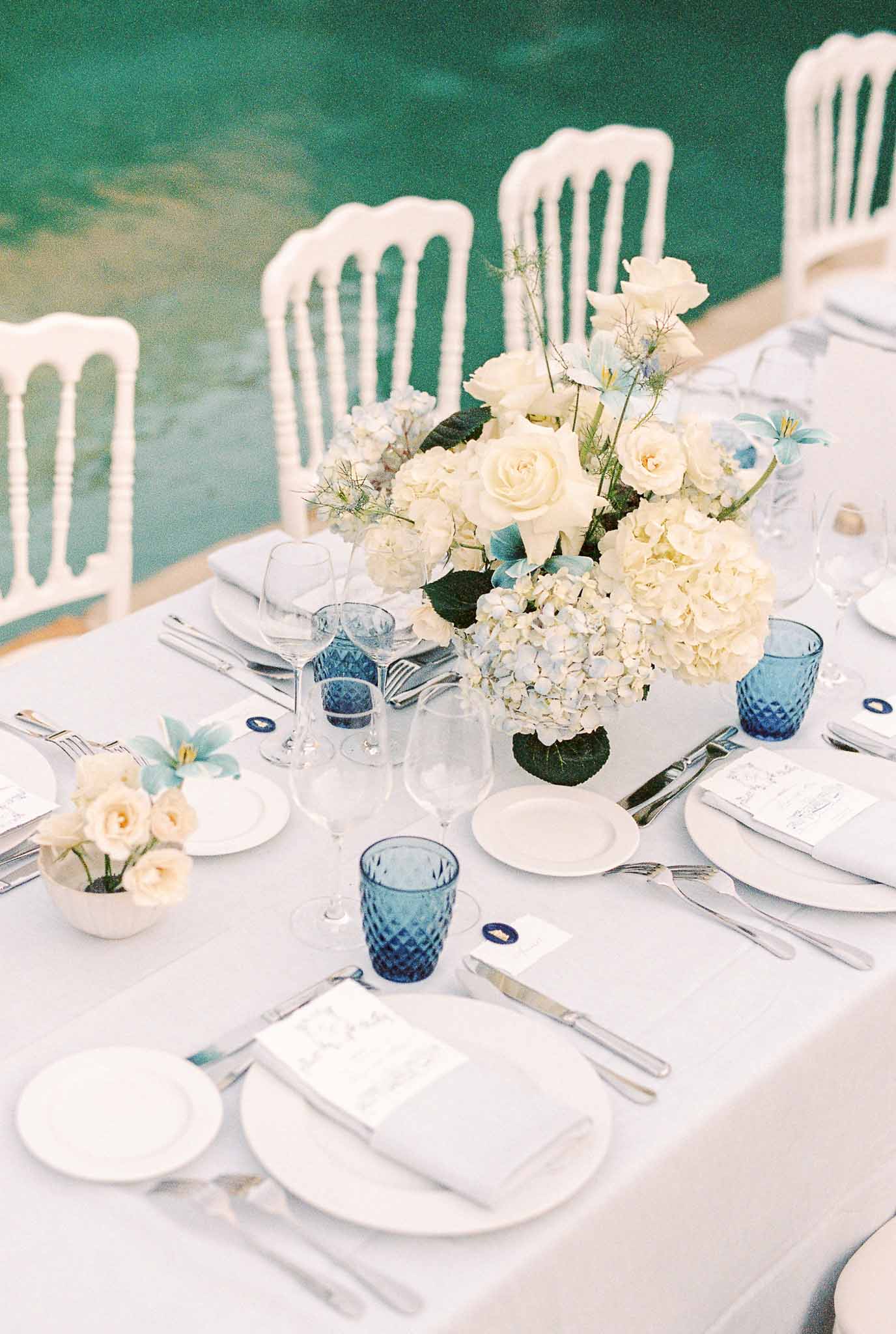 Waterside reception table setting with white linens and blue glassware at outdoor wedding venue