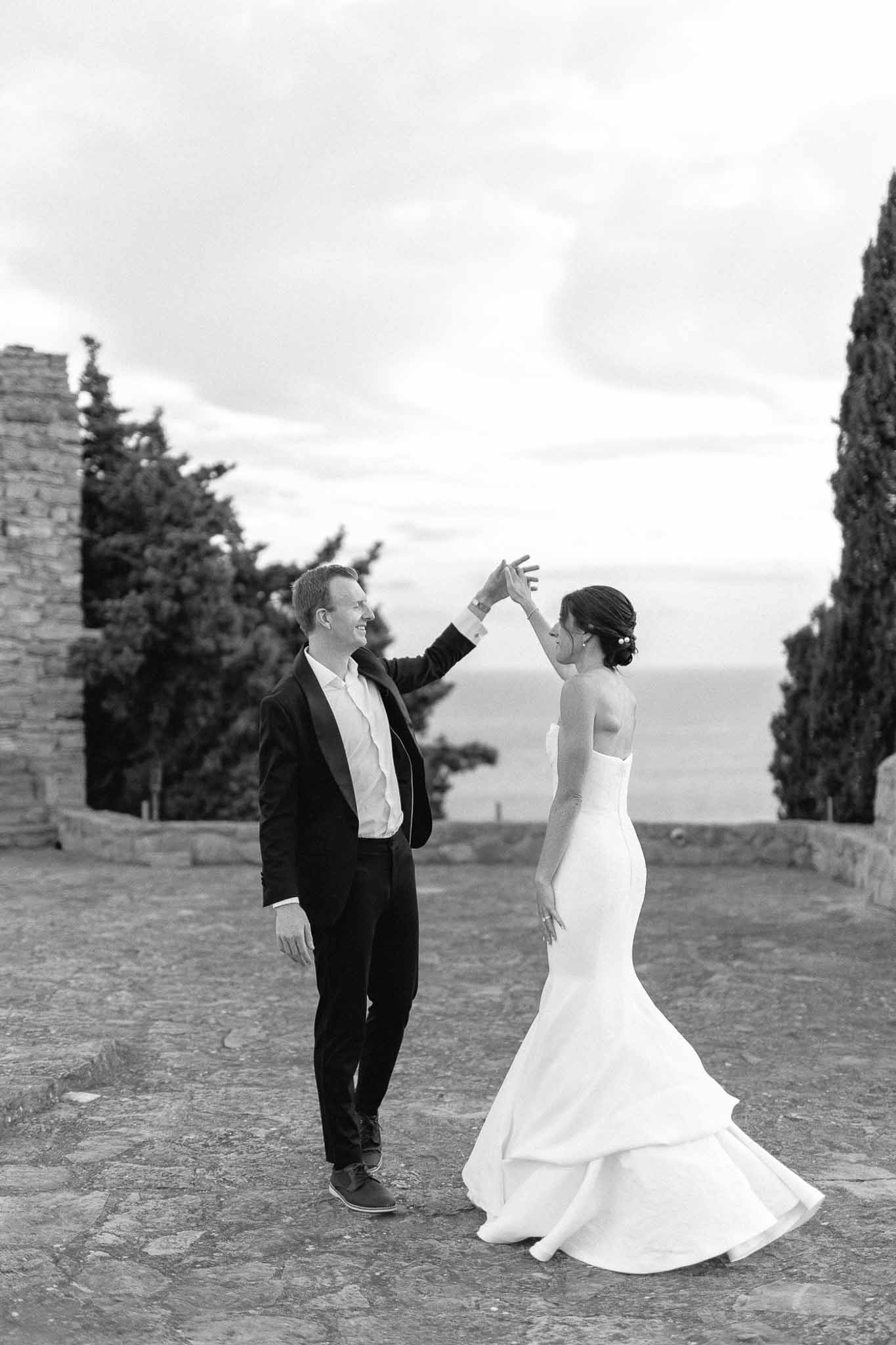 Bride and groom dancing on stone pathway with cypress trees at Mediterranean wedding venue