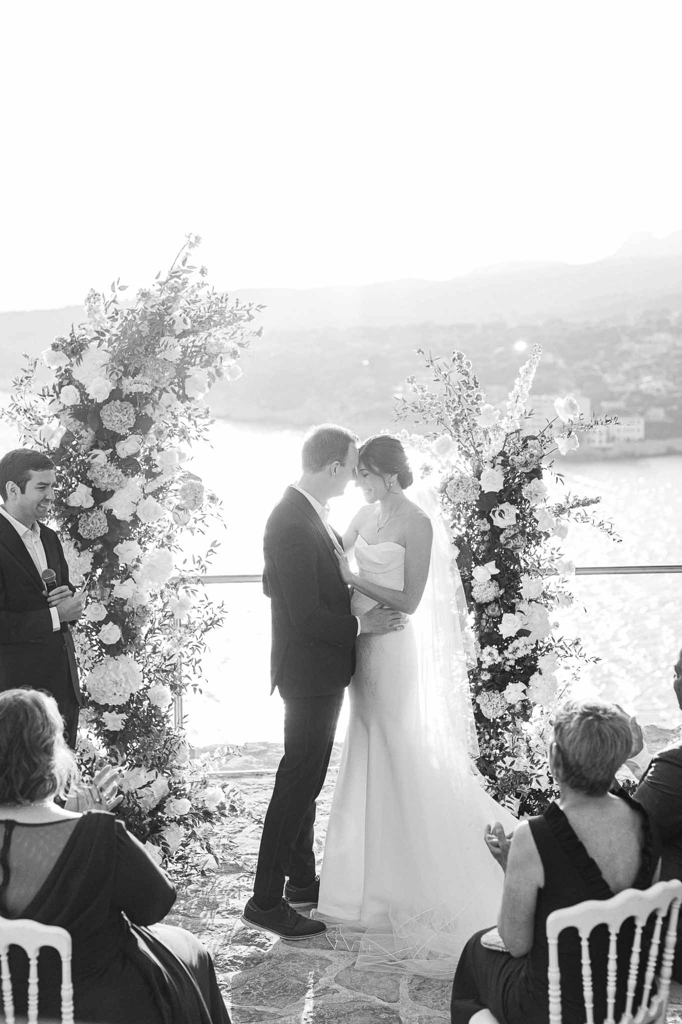 Wedding ceremony with couple exchanging vows on lakeside terrace with floral installations
