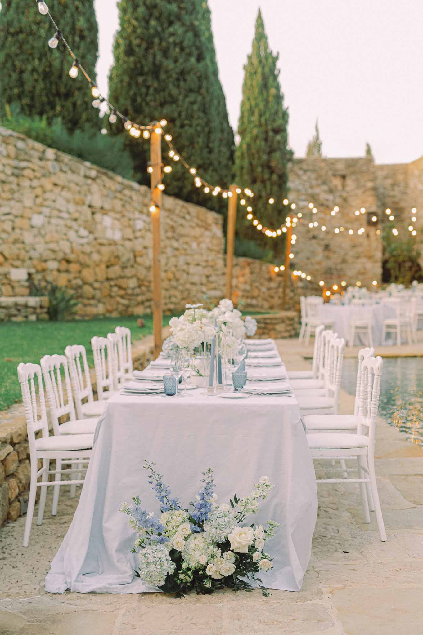 Outdoor reception table setting with floral centerpiece in stone courtyard with string lights