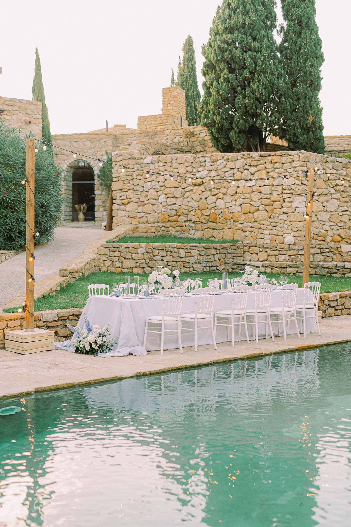 Lavender wedding reception table setup beside pool at Mediterranean stone venue with cypress trees