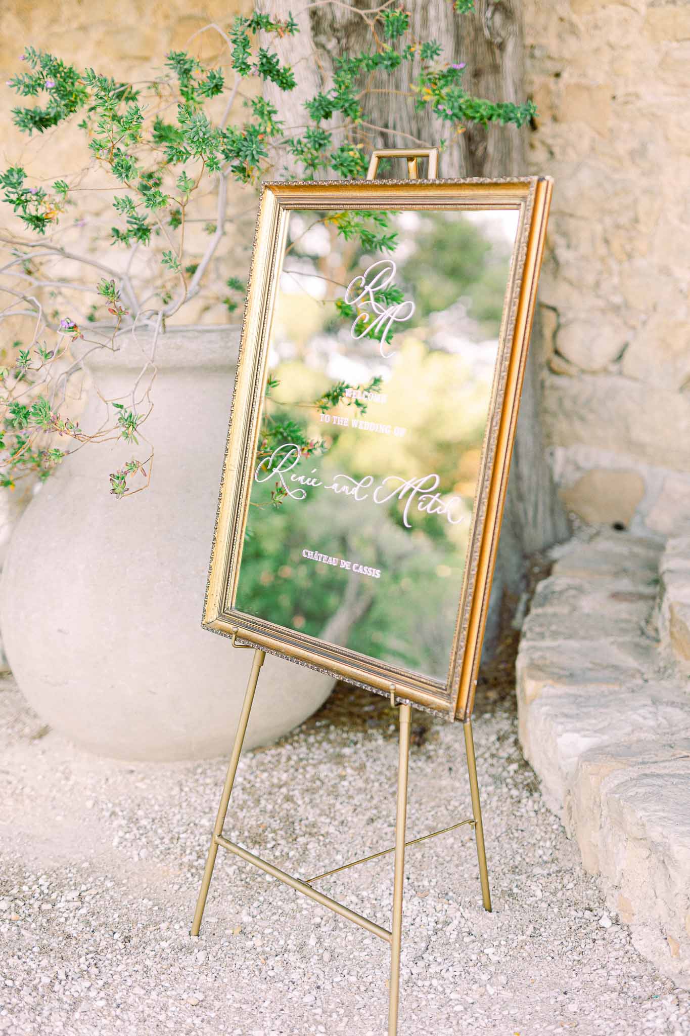 Mirrored welcome sign with gold frame and botanical arrangement at château courtyard entrance
