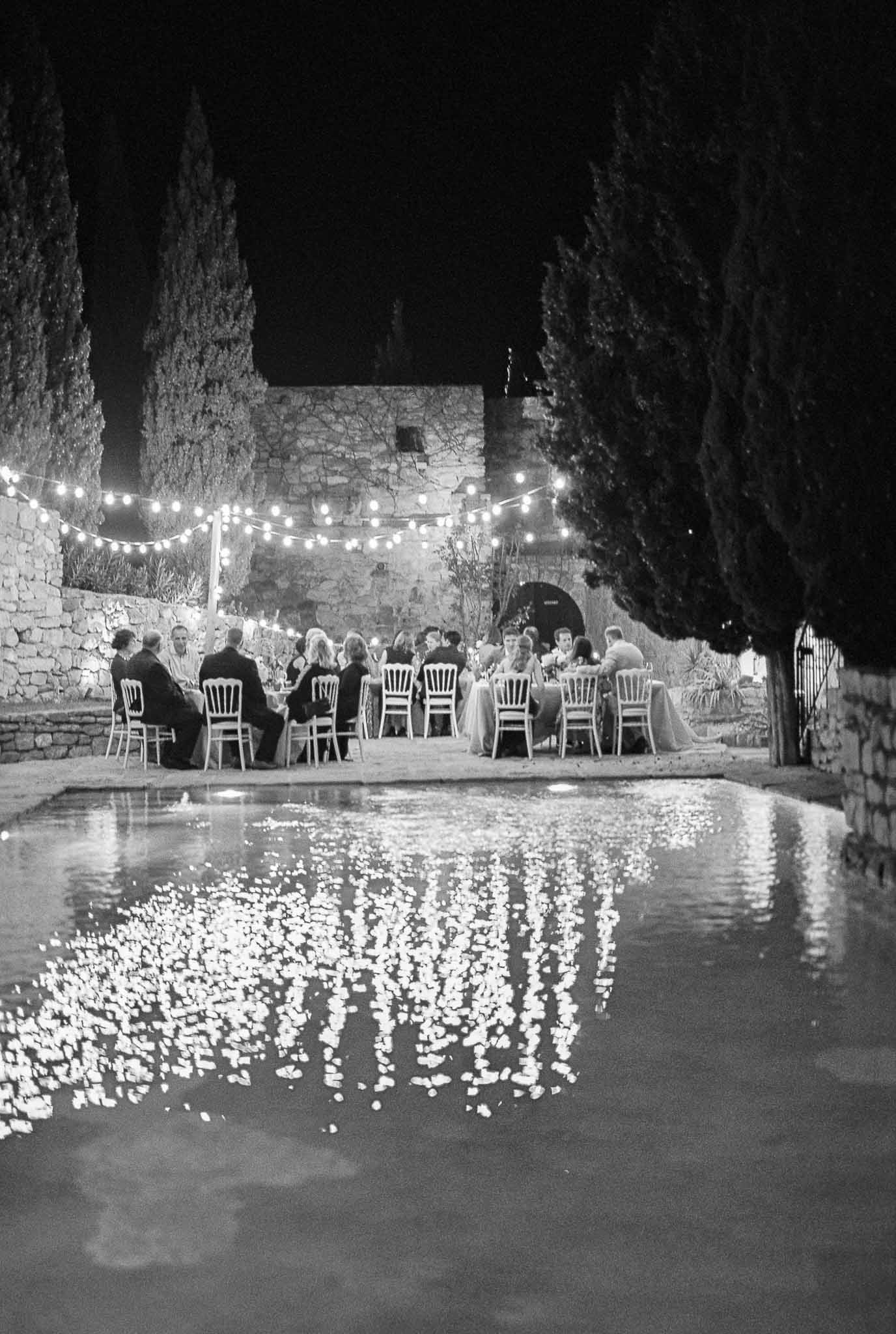 Nighttime wedding reception dinner in historic stone courtyard with string lights and cypress trees