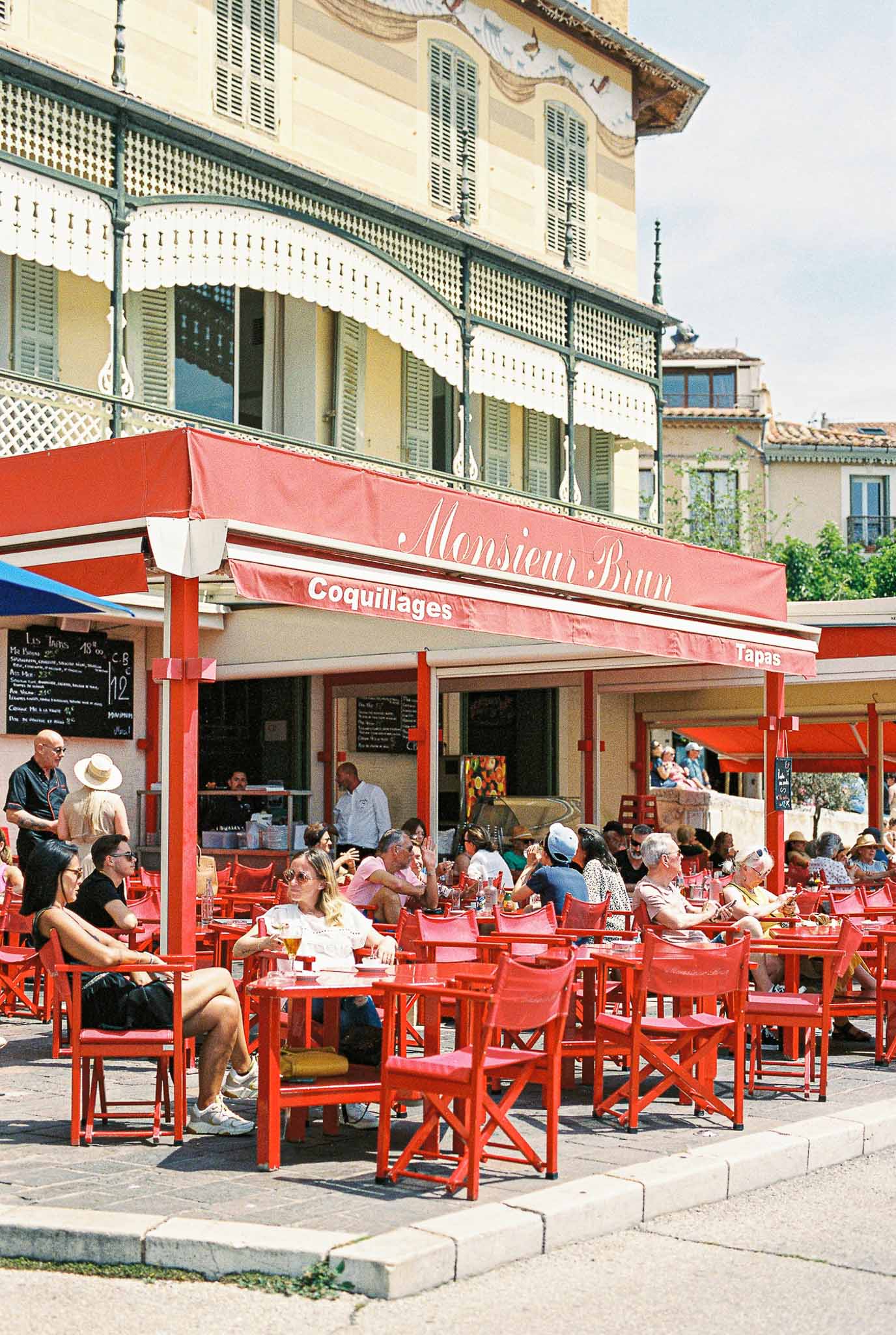 Outdoor cocktail reception at French bistro restaurant with red awning and Mediterranean architecture