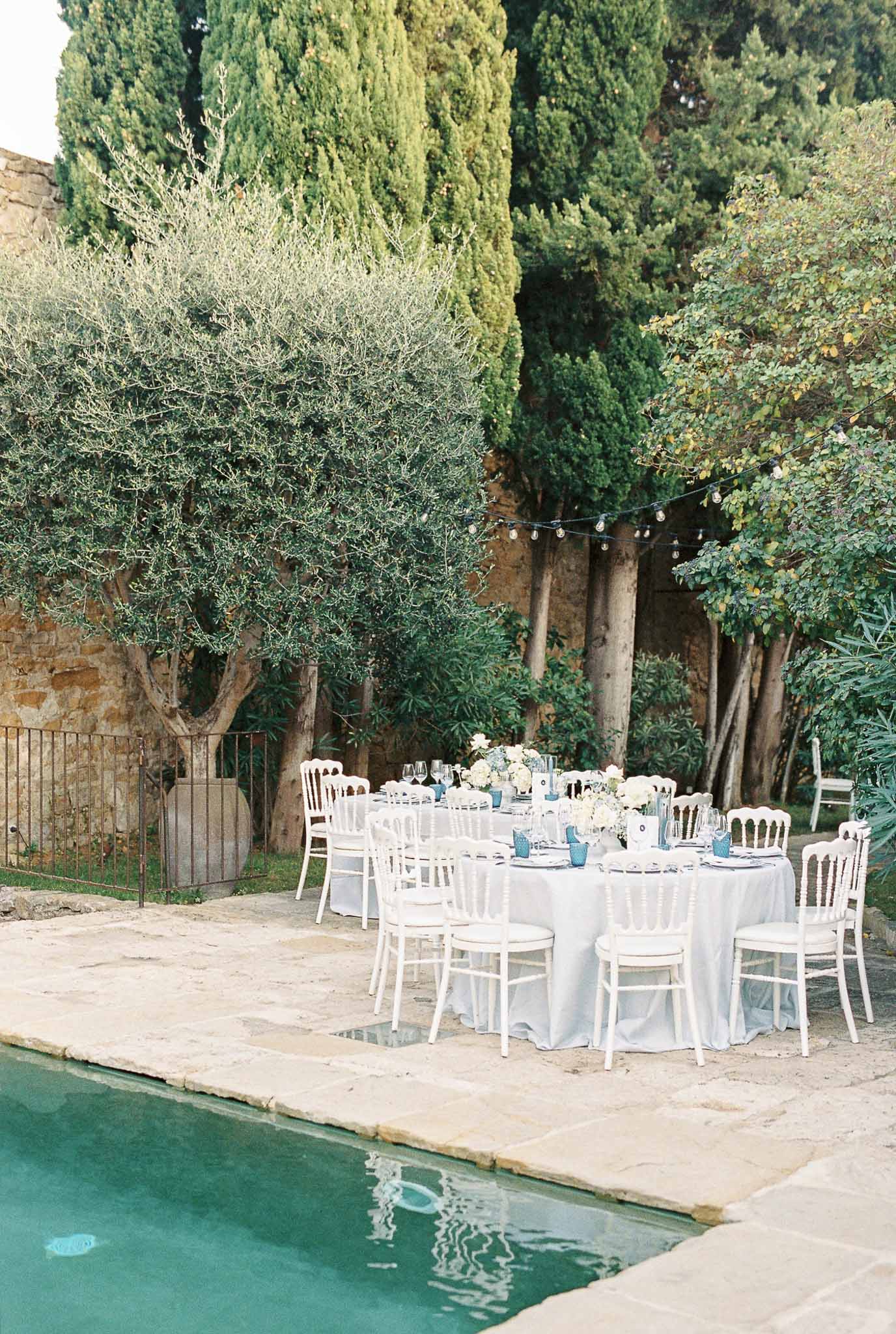 Outdoor wedding reception setup poolside at Mediterranean villa with white tables and blue napkins