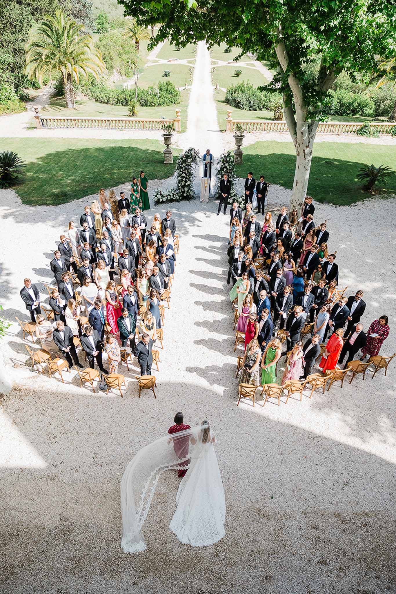Aerial view of outdoor wedding ceremony at formal garden estate with guests in chiavari chairs