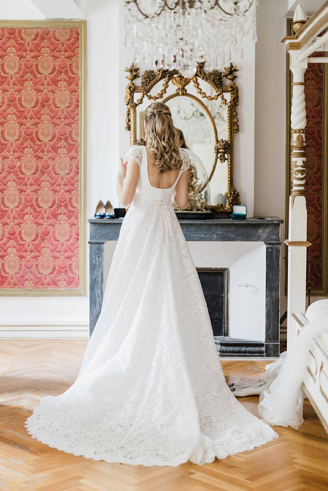 Bride in ivory lace gown looking in ornate mirror during getting ready in elegant bridal suite