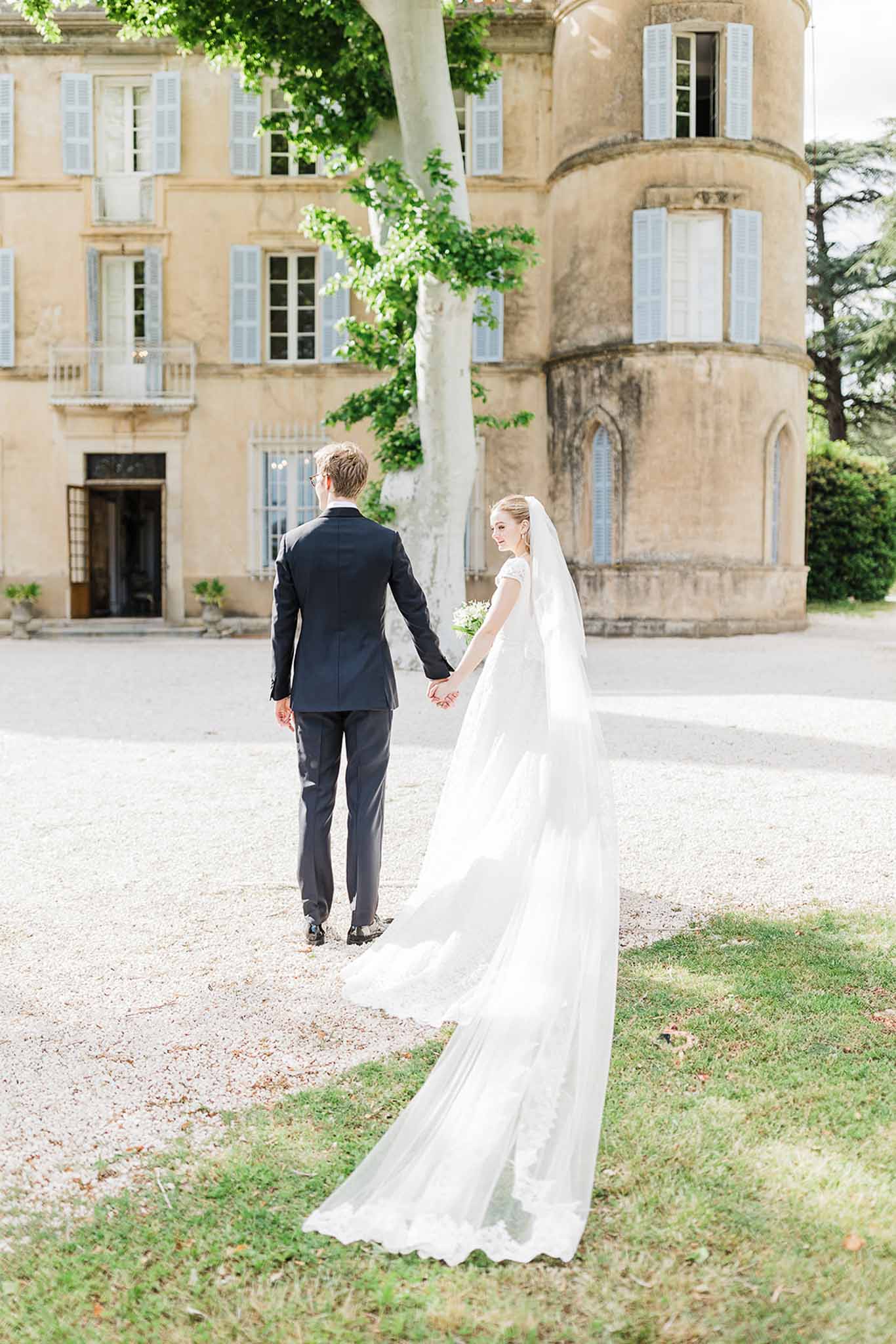 Bride and groom walking hand in hand across château courtyard in French countryside setting