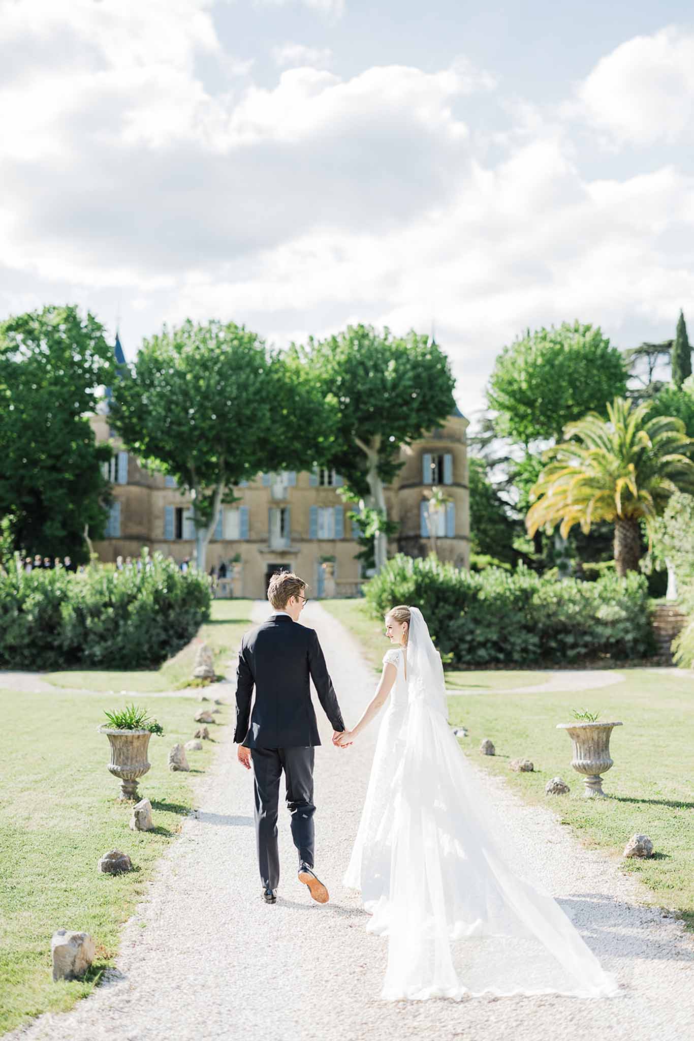 Bride and groom walking toward château in formal Mediterranean garden