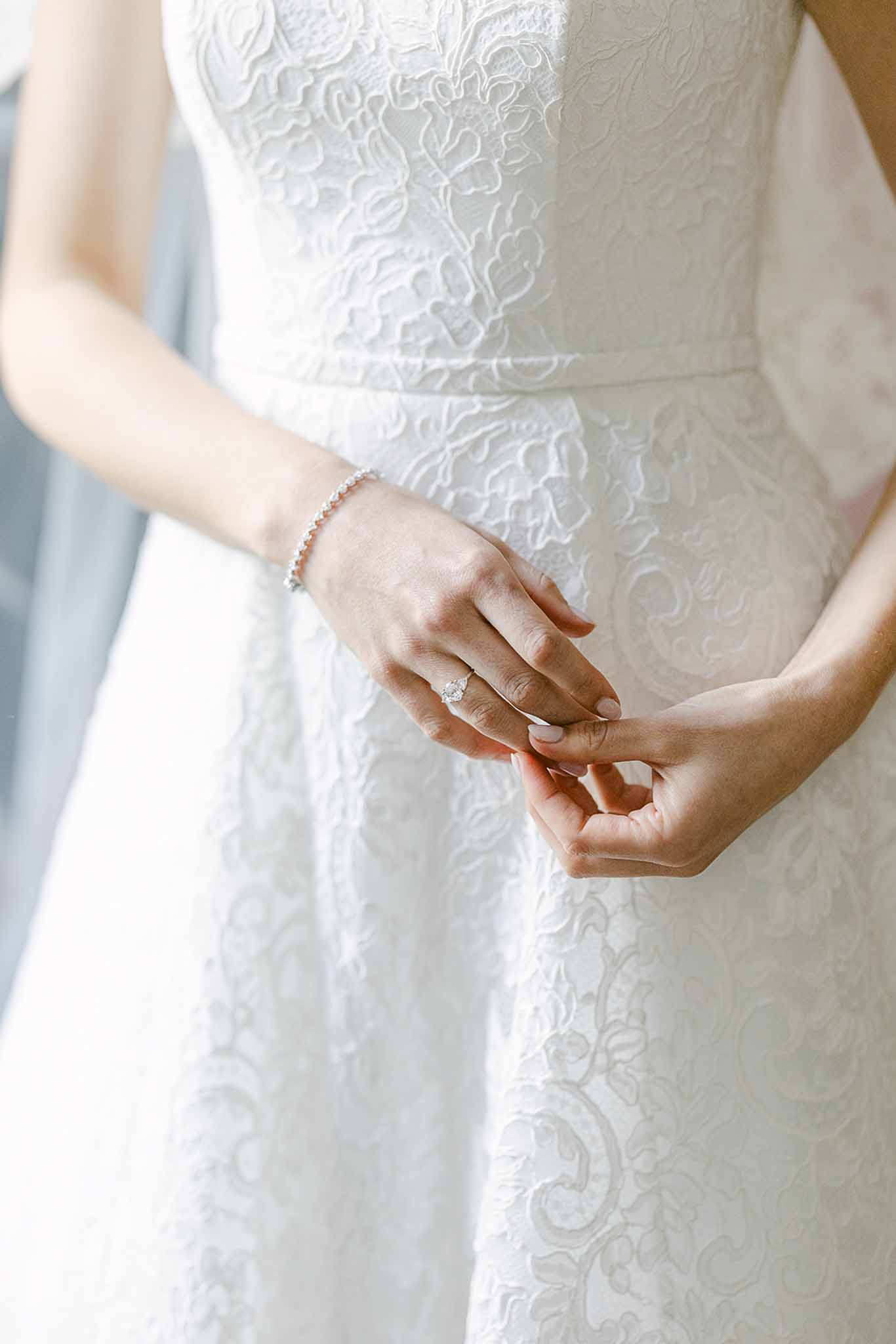 Close-up of bride's hands showing lace wedding dress and diamond ring