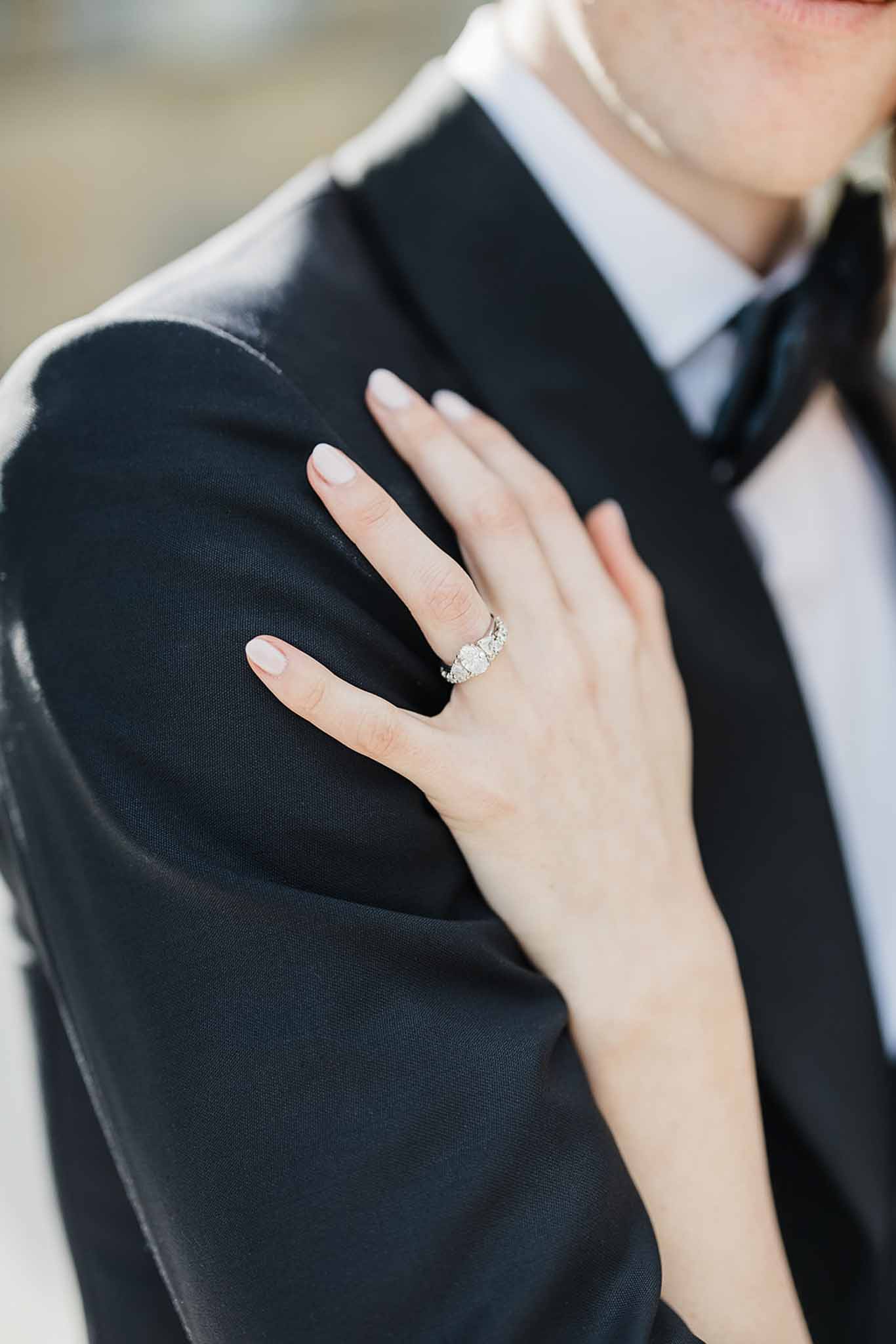 Close-up of bride's hand with engagement ring and wedding band on groom's shoulder at wedding