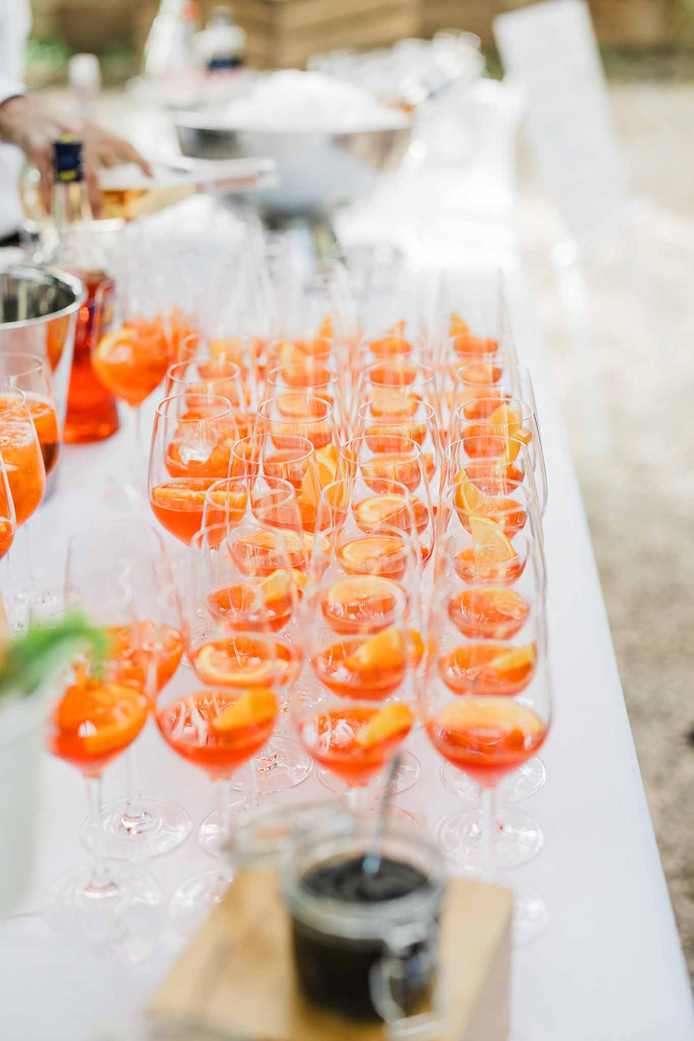 Orange cocktail drinks arranged on white table linens at outdoor wedding cocktail hour