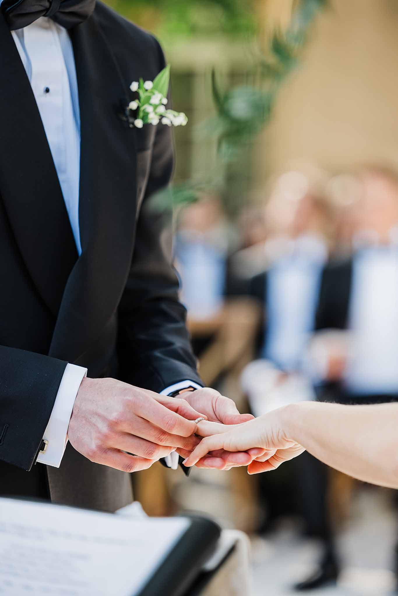 Bride and groom exchanging rings during wedding ceremony with guests in background