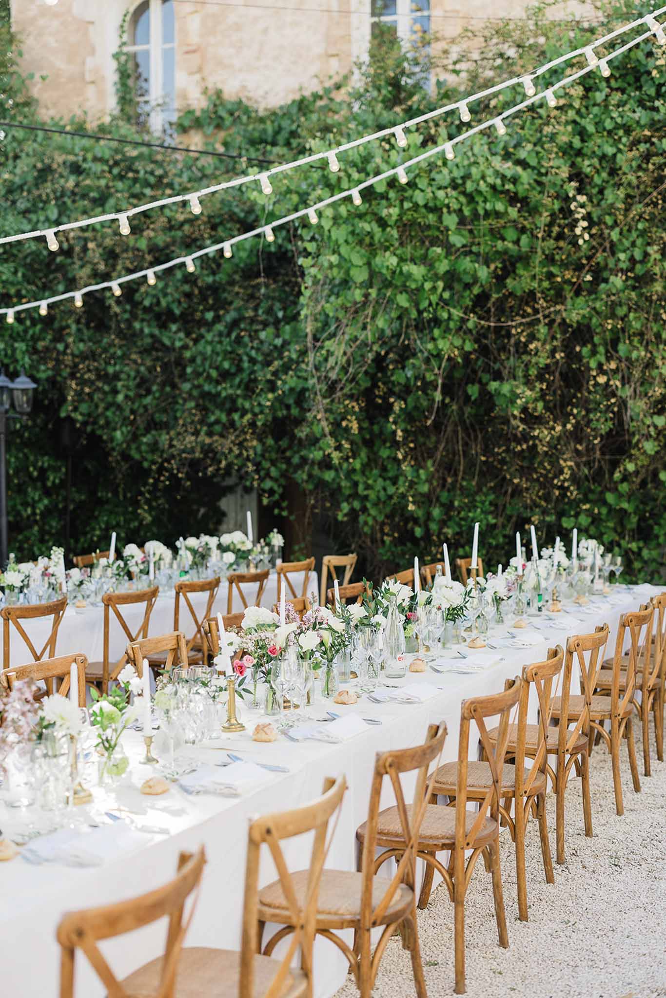 Elegant outdoor reception dinner setup with white linens and floral centerpieces in ivy-covered courtyard