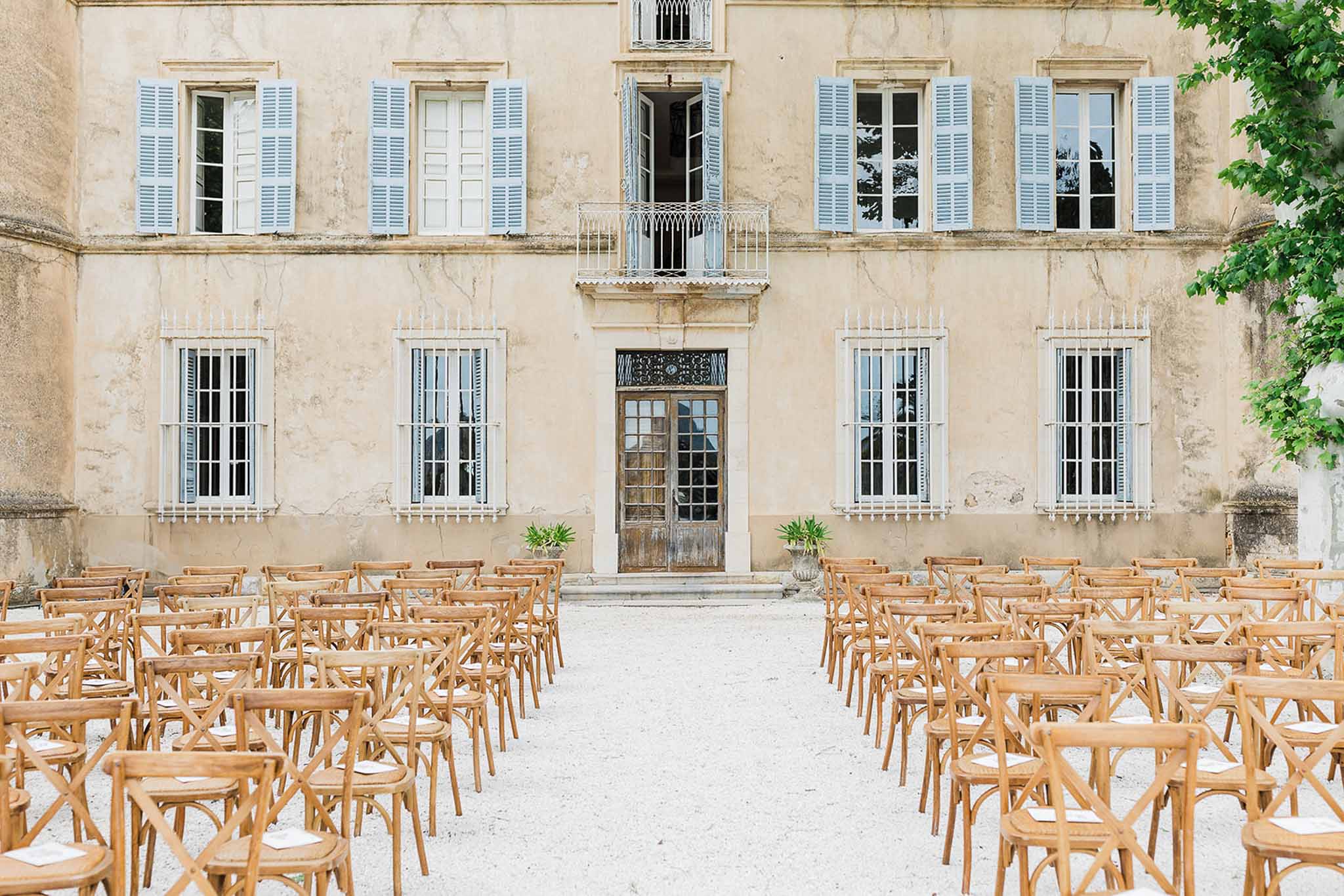 Wedding ceremony setup in courtyard of historic French stone building with crossback chairs