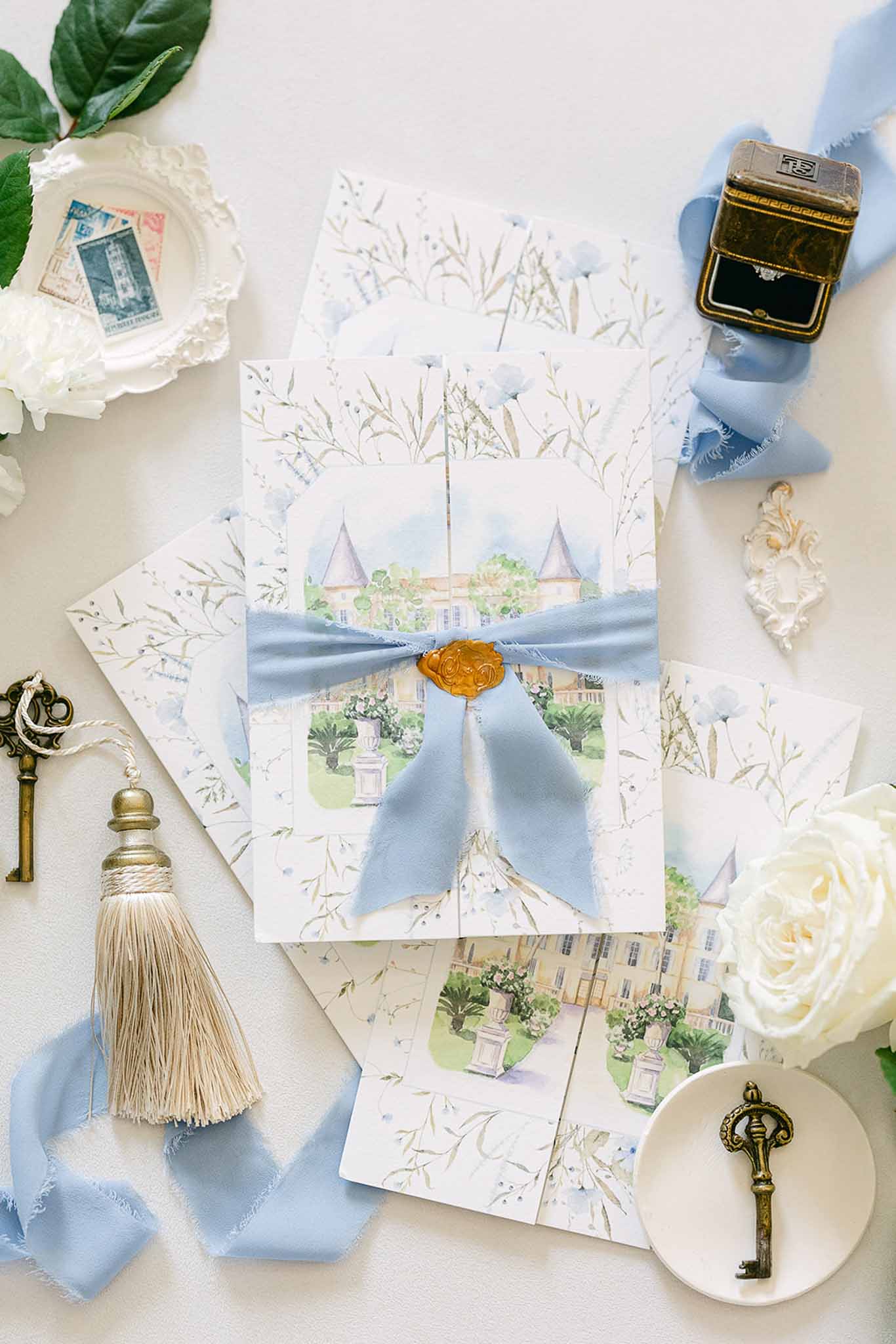 Wedding invitation flat lay with dusty blue ribbon and vintage styling elements on neutral surface