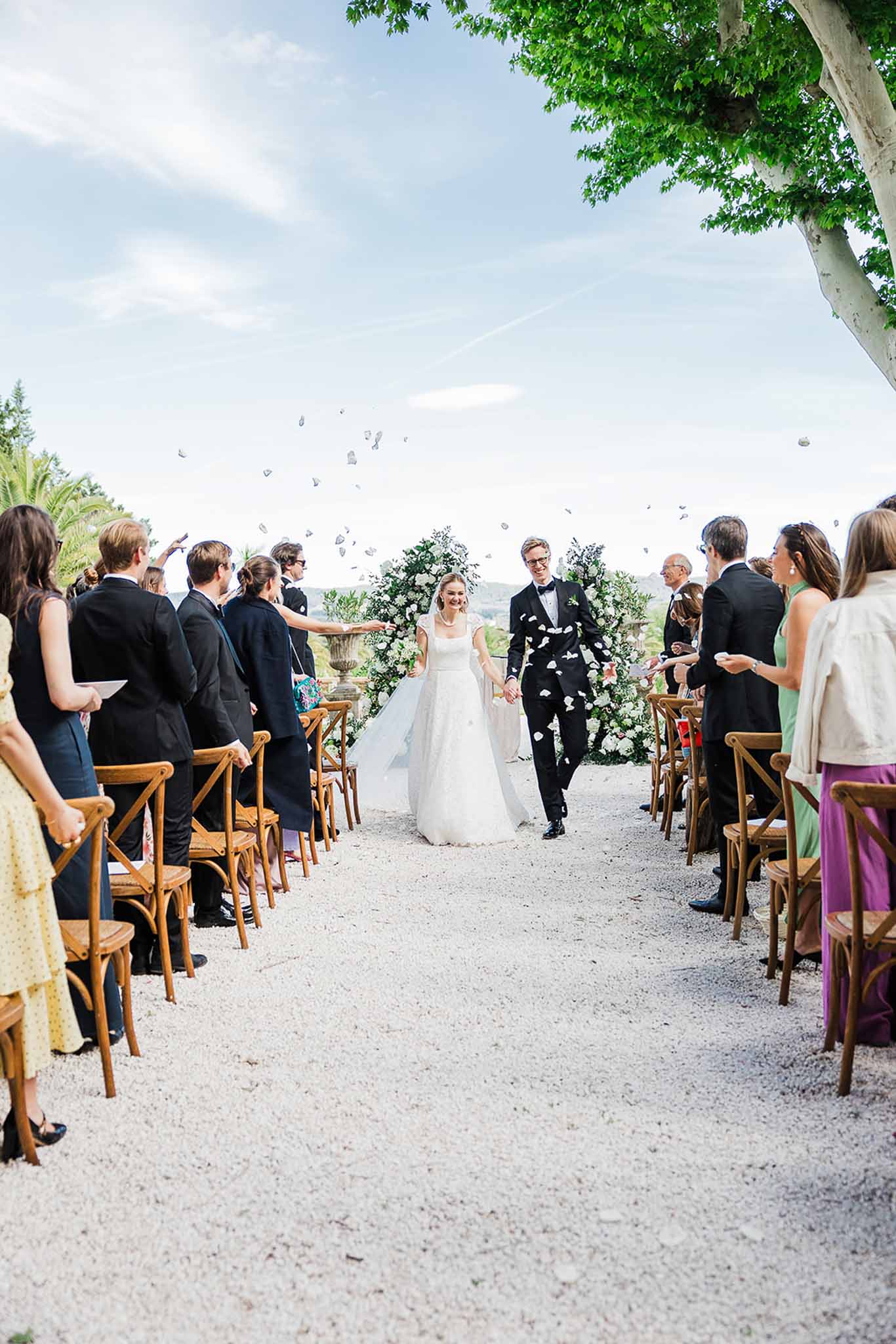 Bride and groom walking down aisle after outdoor ceremony with guests throwing petals at garden wedding venue