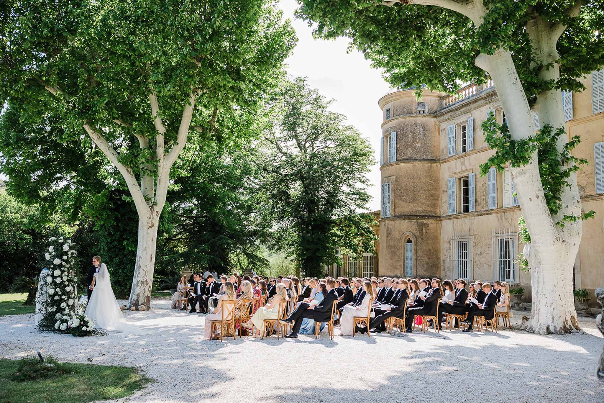Outdoor wedding ceremony in historic château courtyard with guests and couple under plane tree