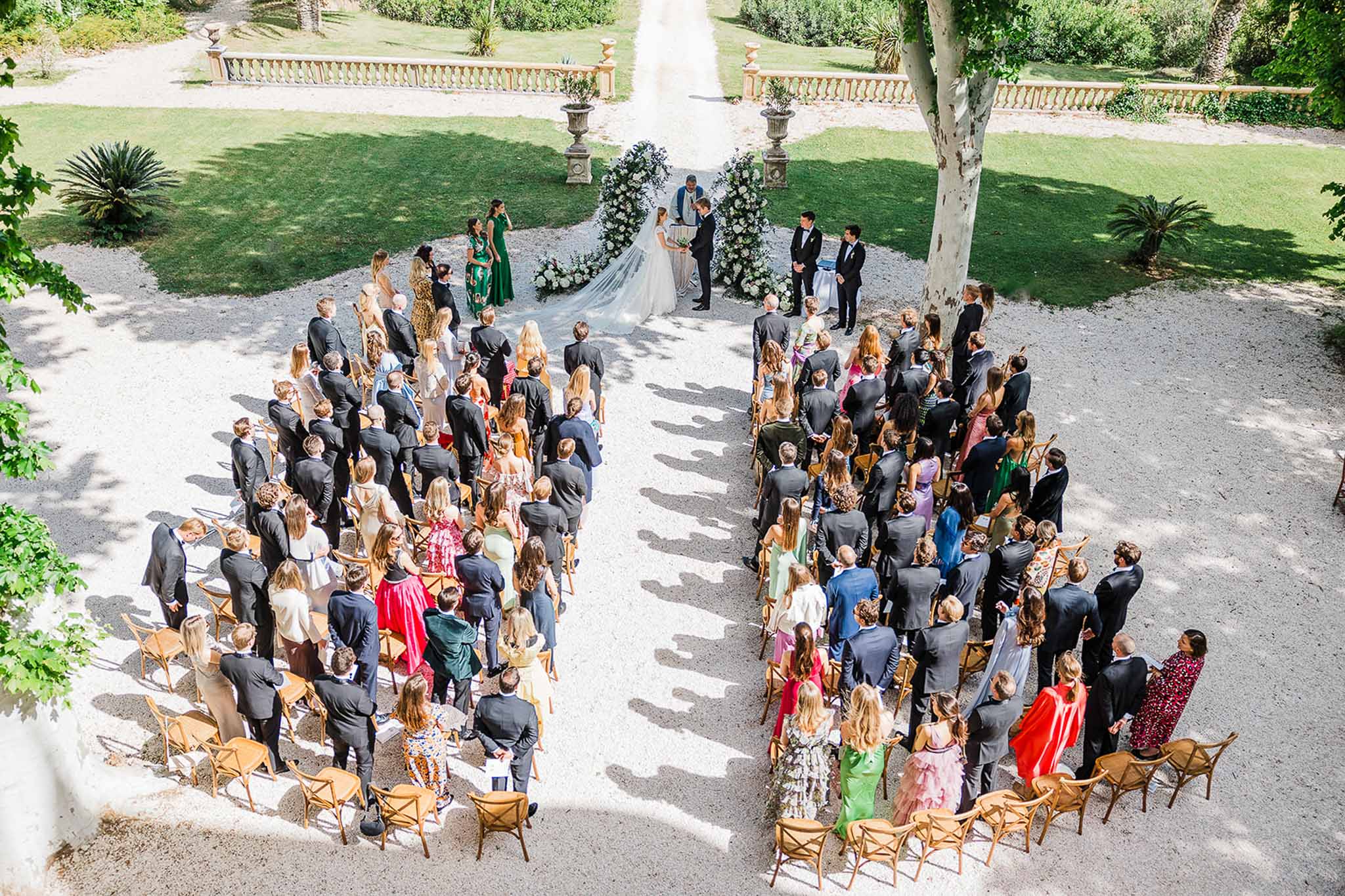 Aerial view of outdoor wedding ceremony in classical French garden with guests seated in formal arrangement