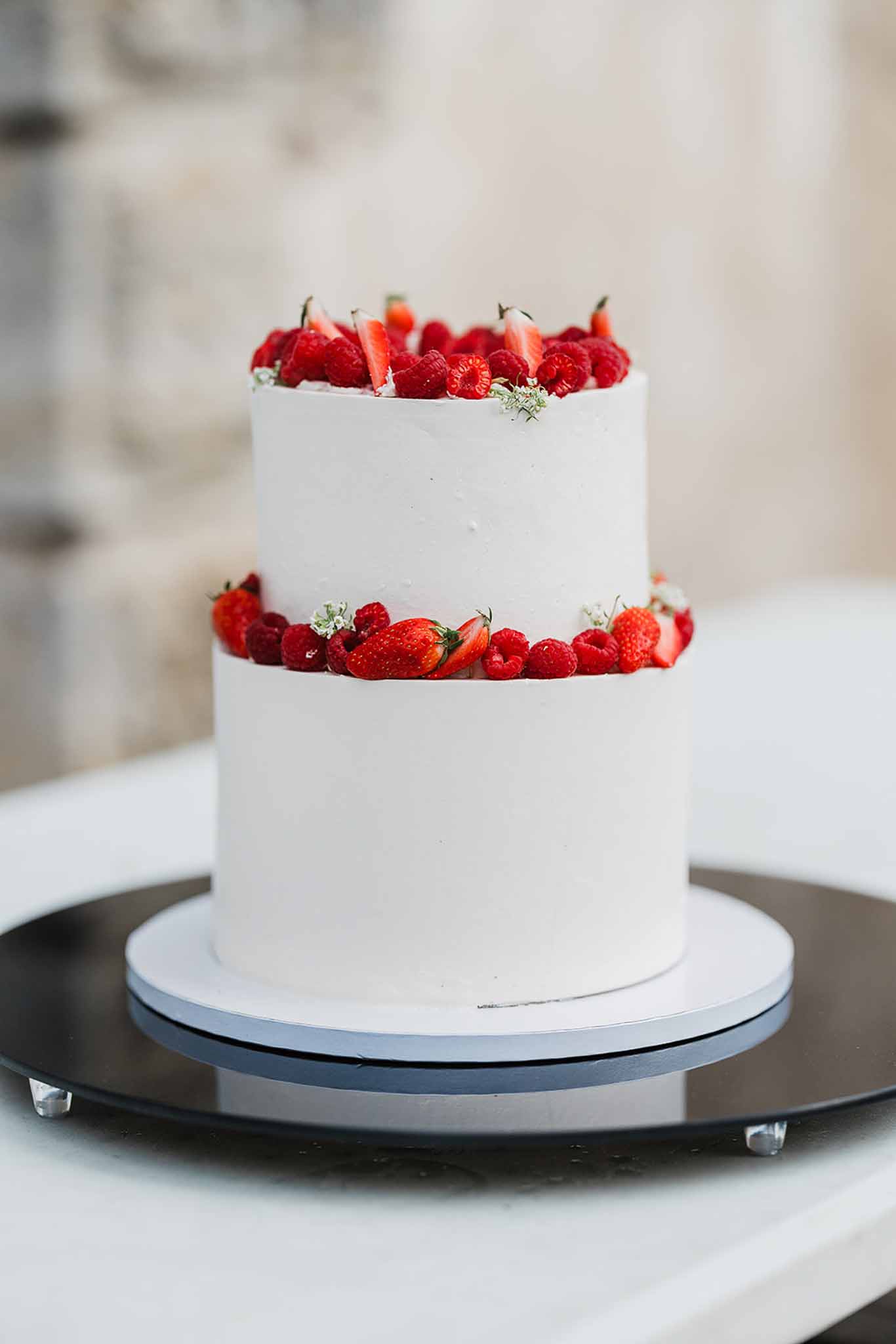 Two-tier wedding cake with white frosting, red berries, and baby's breath on black cake stand