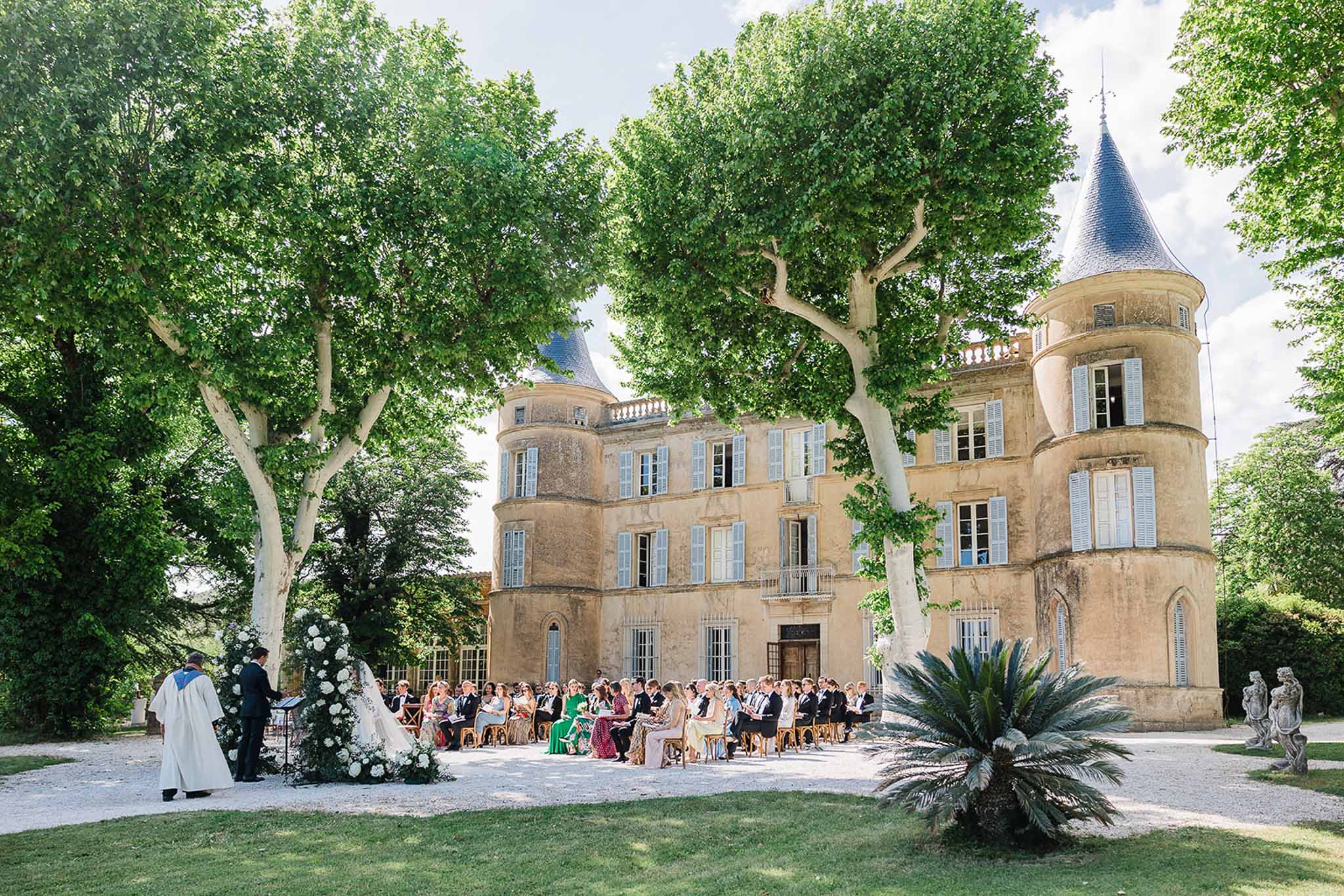 Wedding ceremony in château courtyard with guests and floral arch