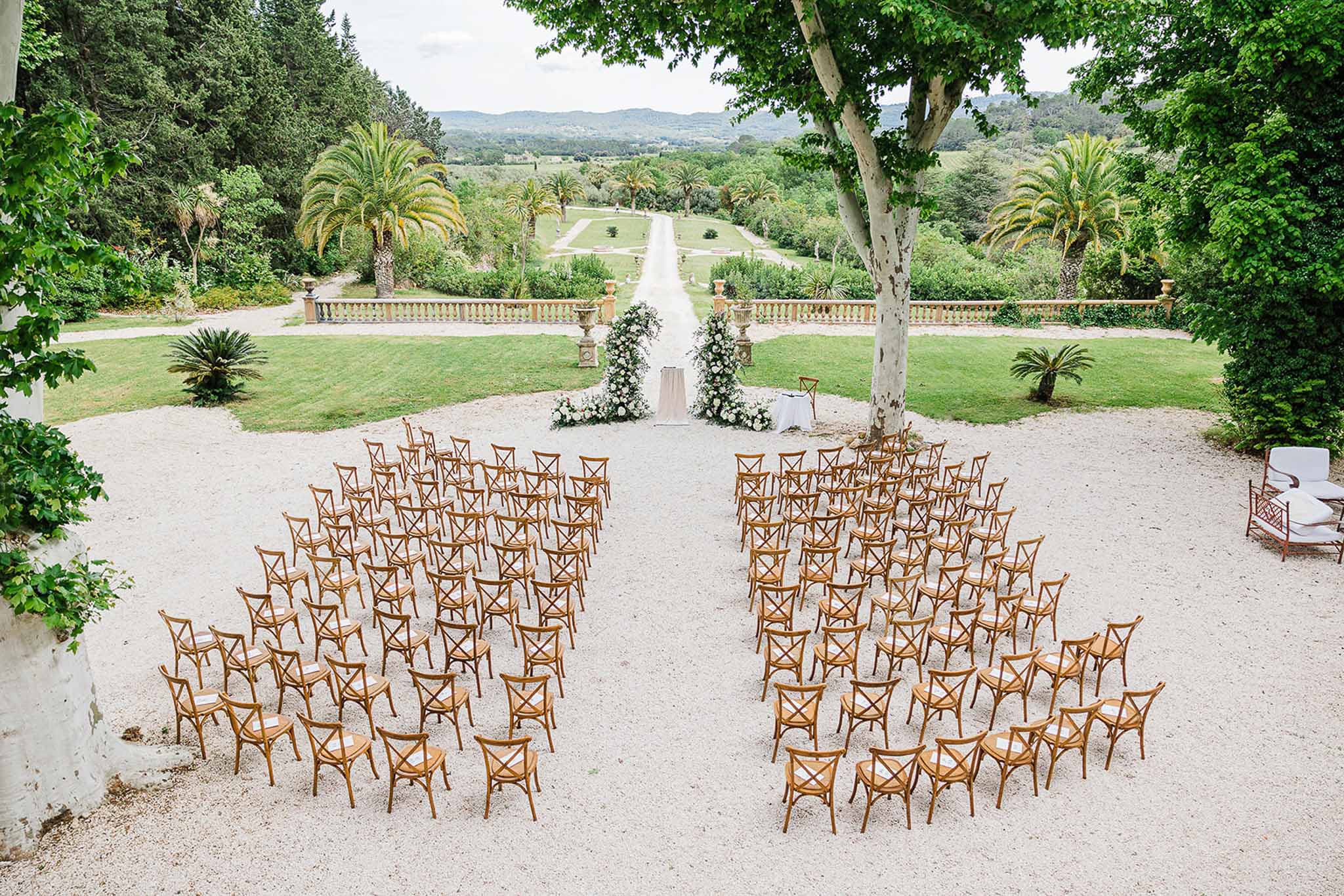 Wedding ceremony setup in Mediterranean estate garden with wooden chairs and white altar arrangements