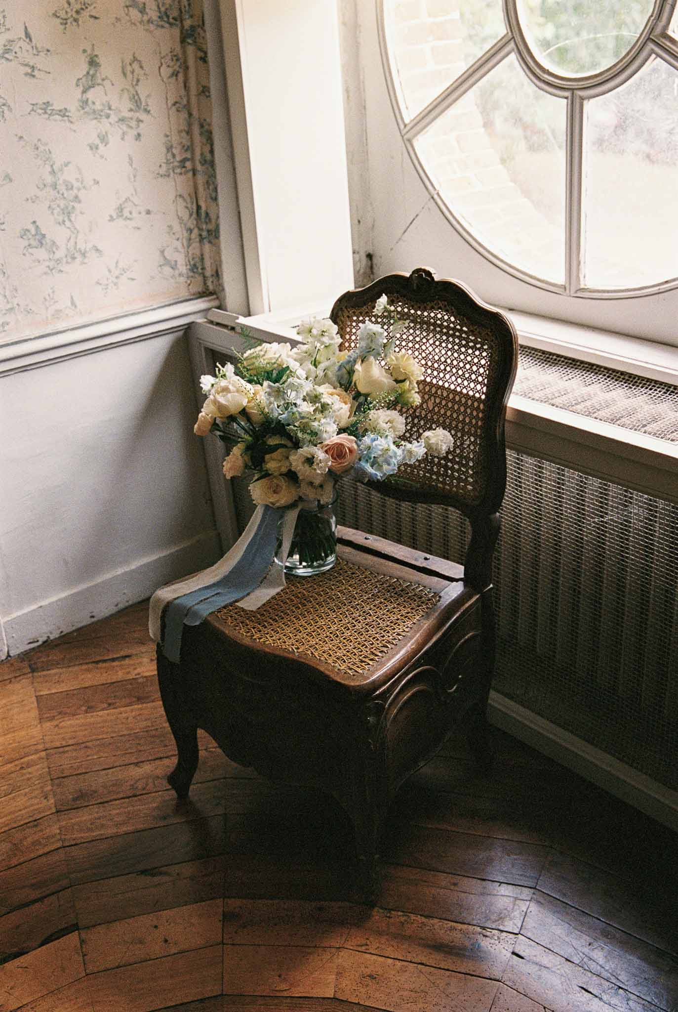 Bridal bouquet with cream and dusty rose flowers on vintage chair by arched windows in getting ready room