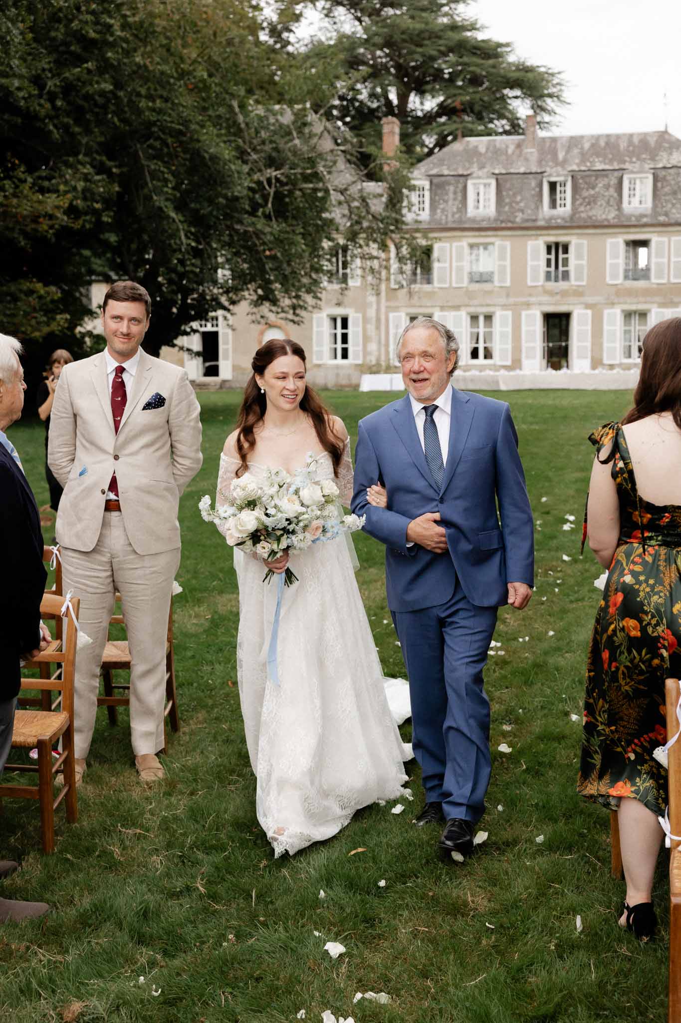 Bride walking down aisle with father during outdoor ceremony at French chateau garden