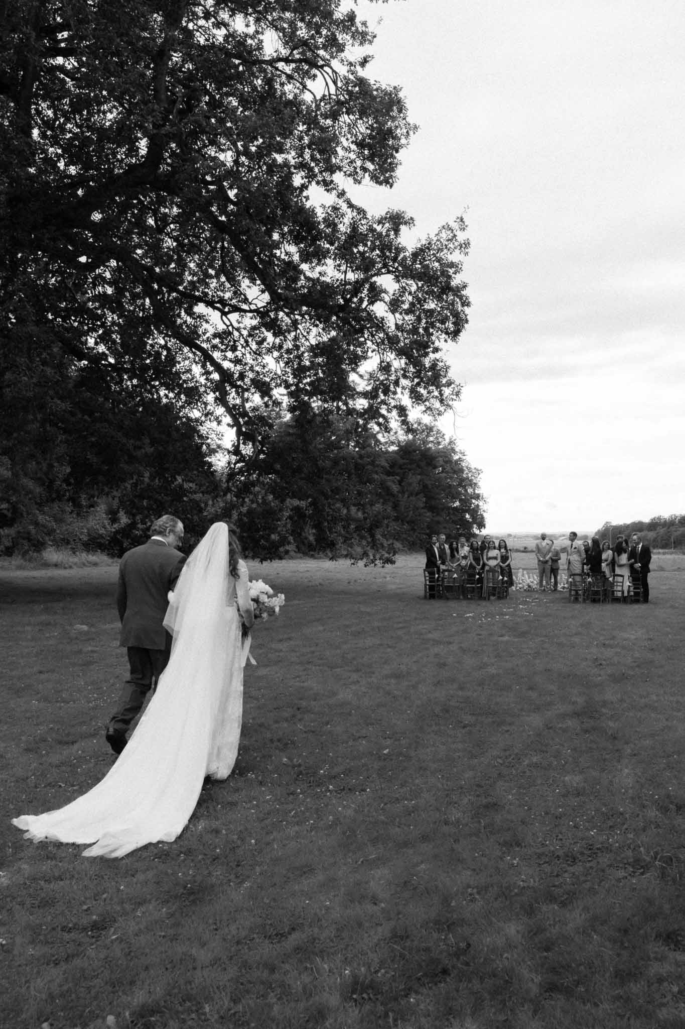 Bride walking with father during outdoor ceremony processional in countryside field