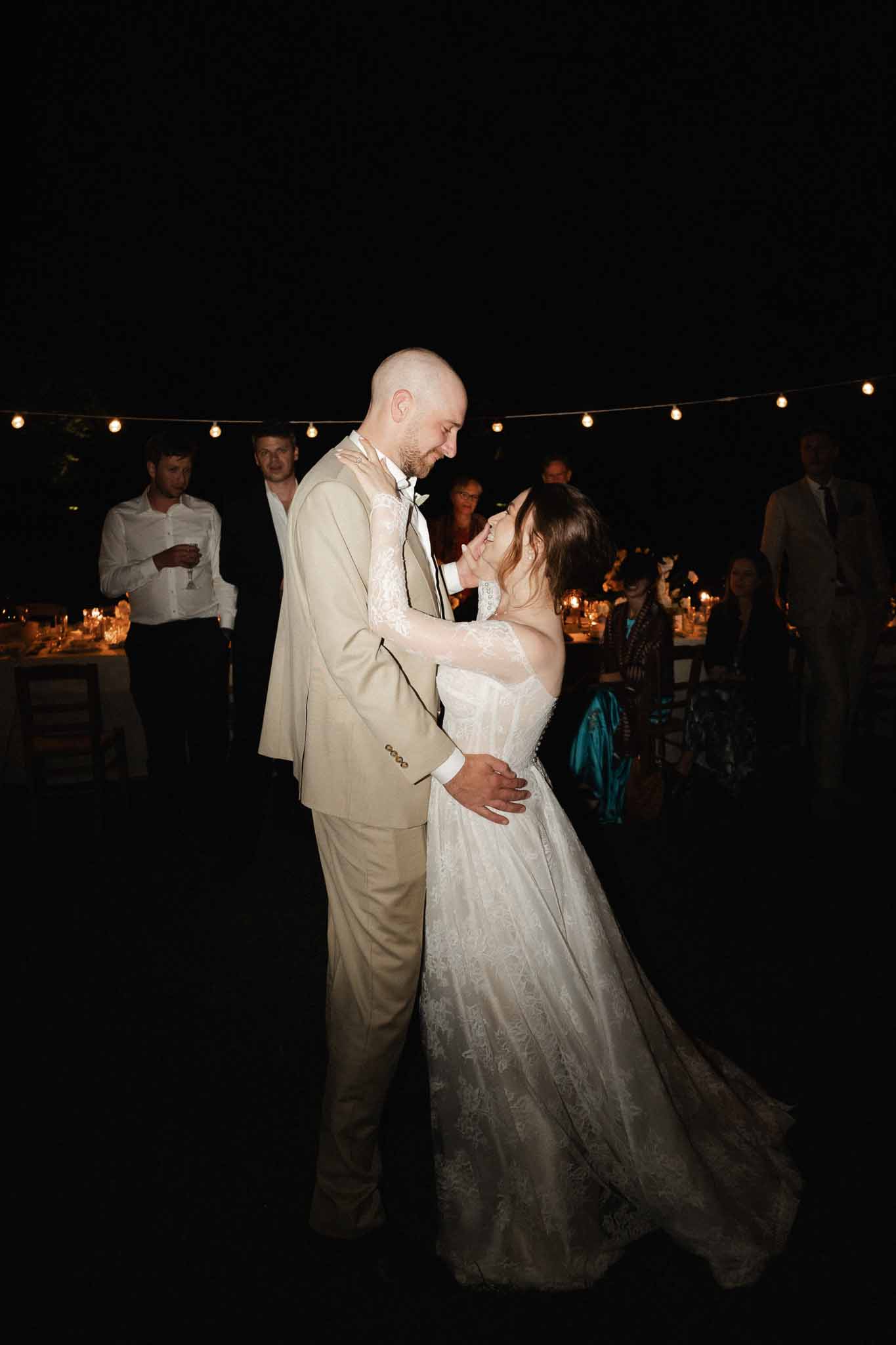 Bride and groom first dance at outdoor evening wedding reception under string lights