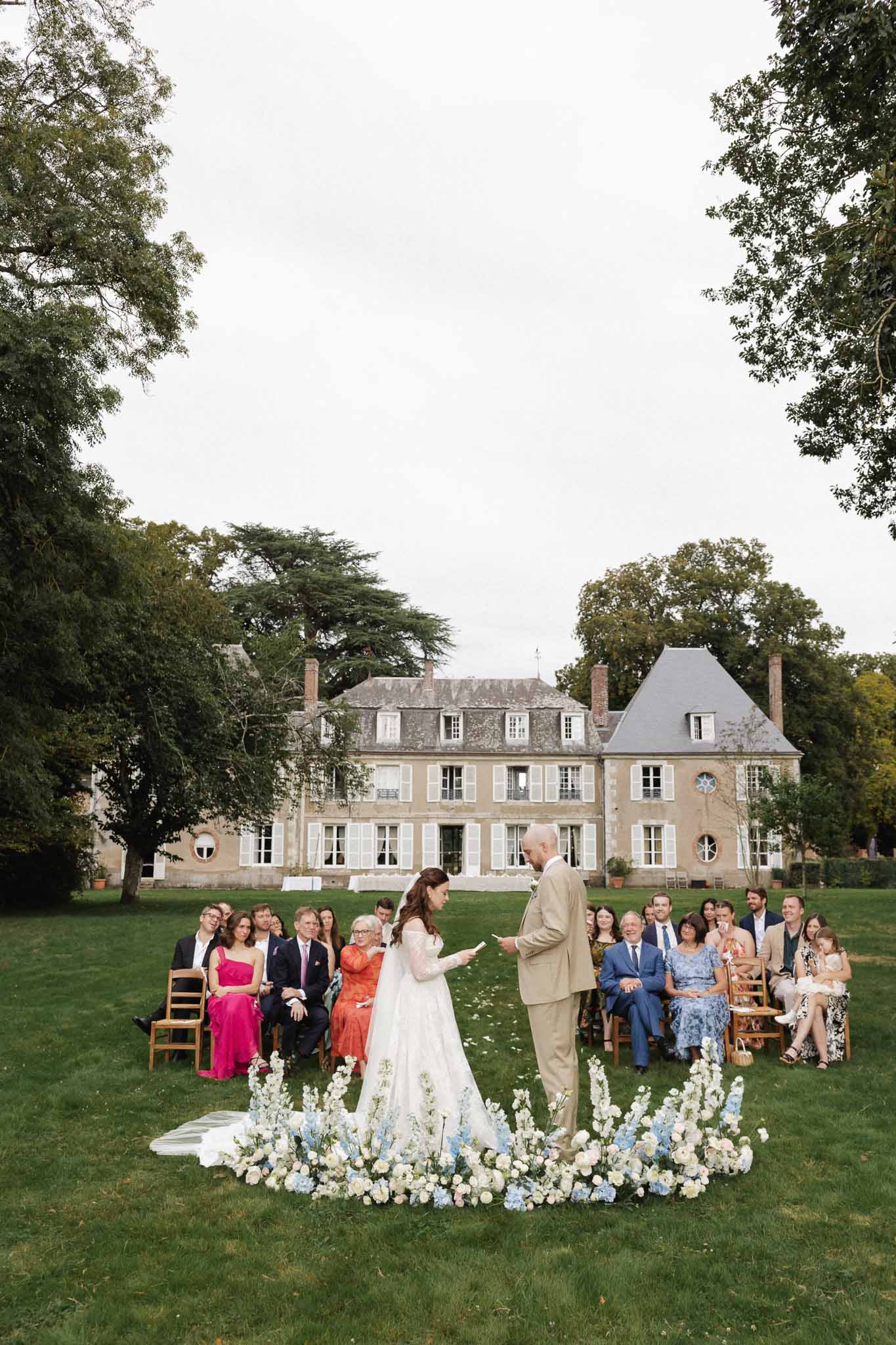 Outdoor wedding ceremony with bride and groom exchanging vows at French château with guests seated on lawn