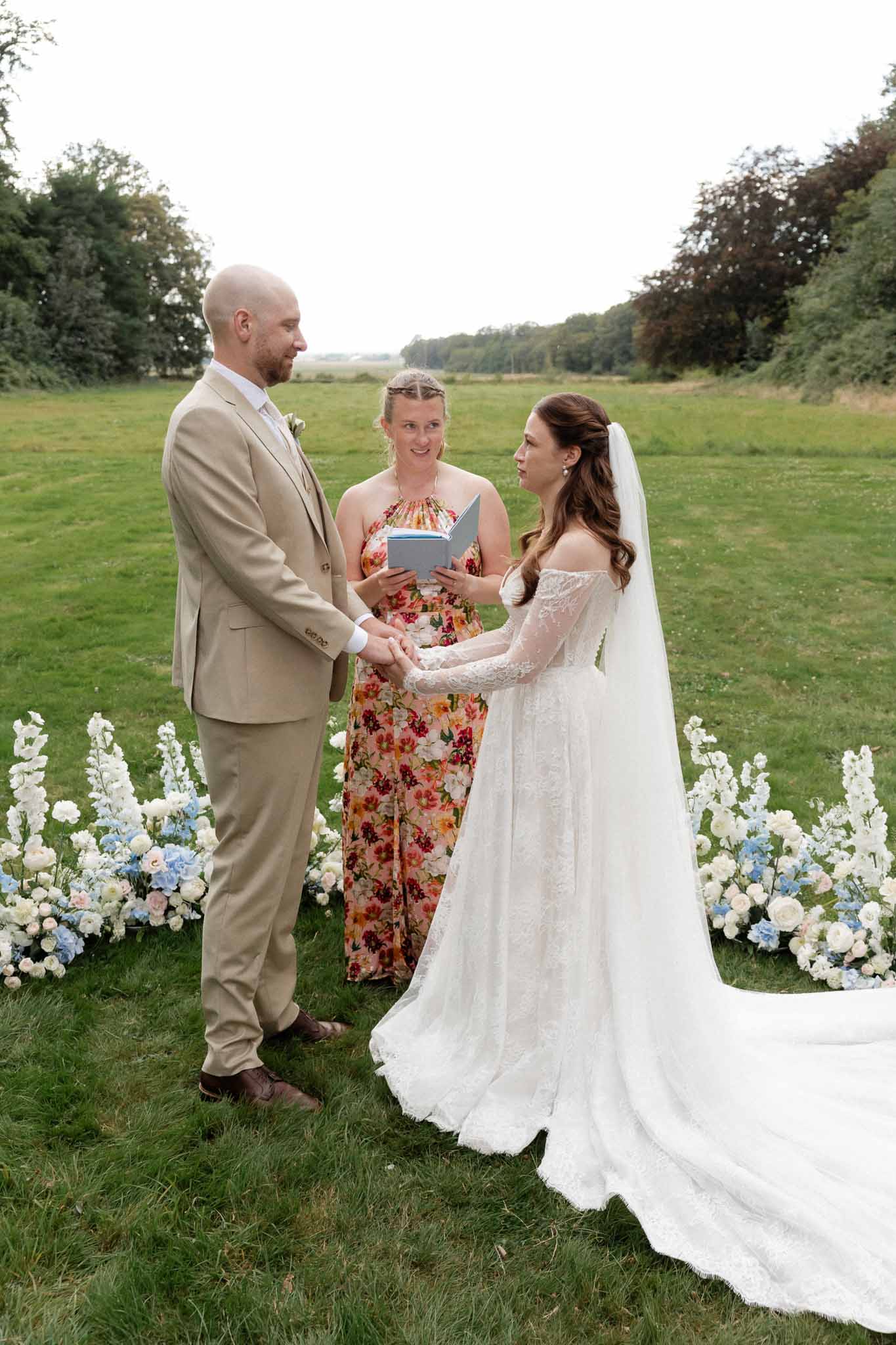 Outdoor wedding ceremony with bride and groom exchanging vows in countryside field with floral arrangements