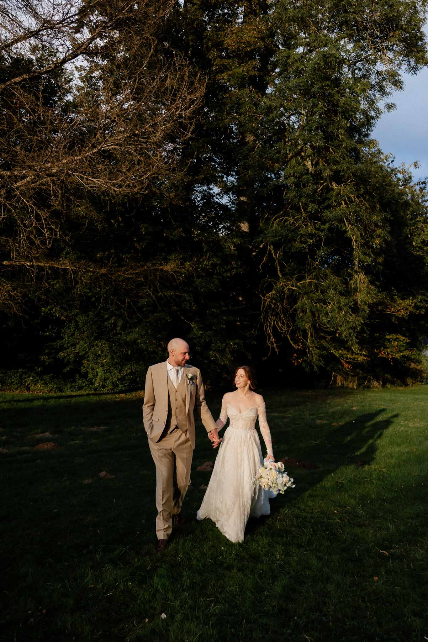 Bride and groom walking hand-in-hand across garden lawn at estate wedding venue