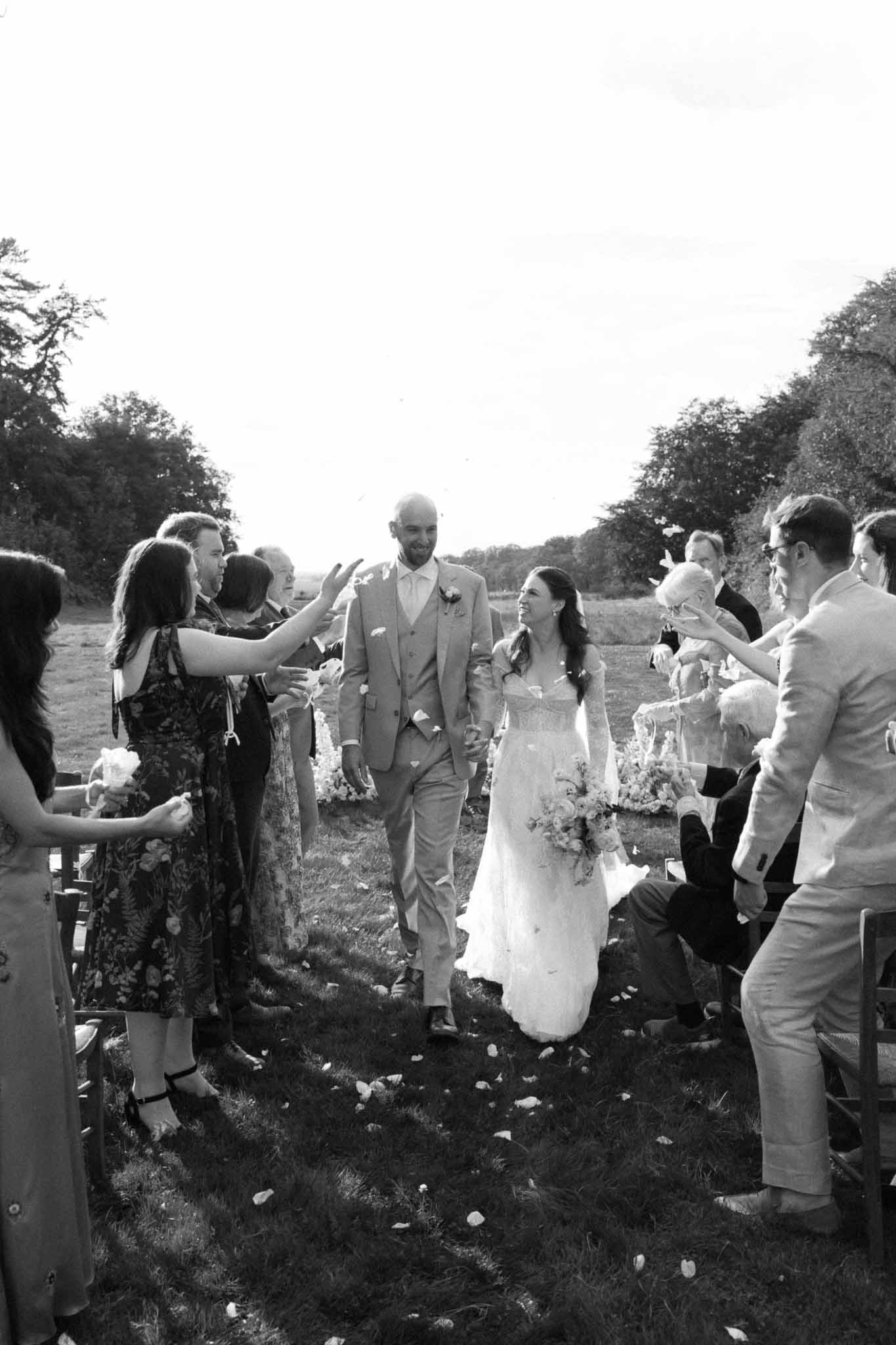 Bride and groom walking recessional through guest line after outdoor ceremony in rural meadow setting