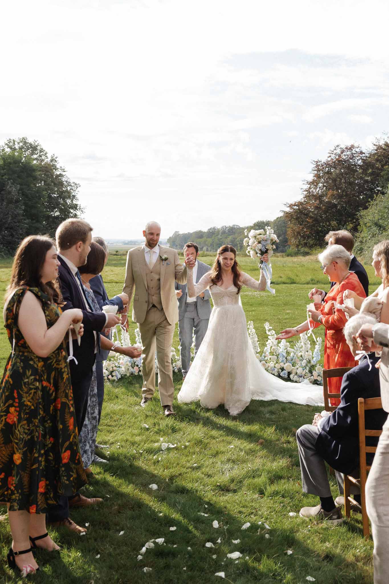 Bride and groom walking down aisle after outdoor ceremony in countryside setting with seated guests