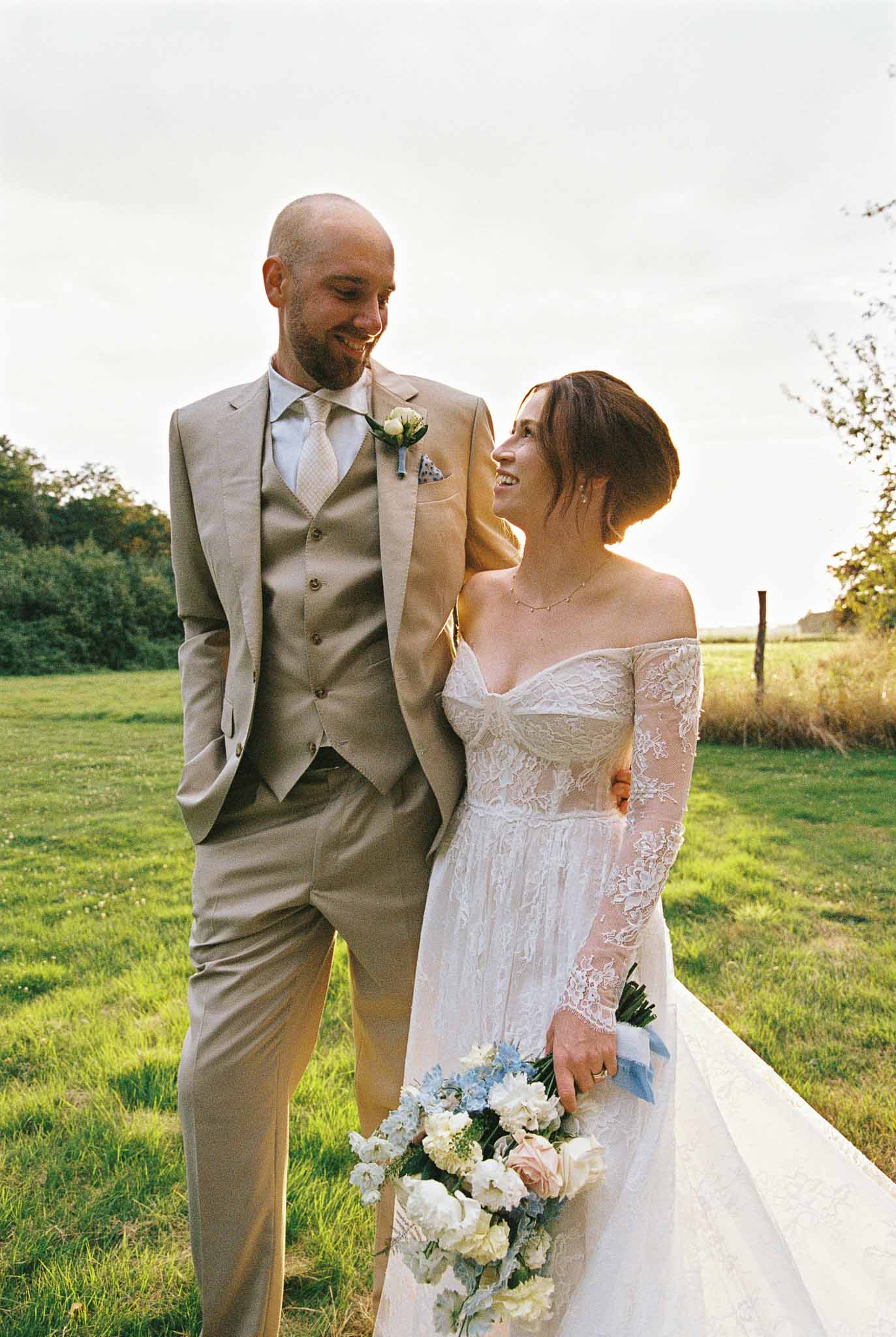 Bride and groom walking together in countryside field with trees and pastoral backdrop