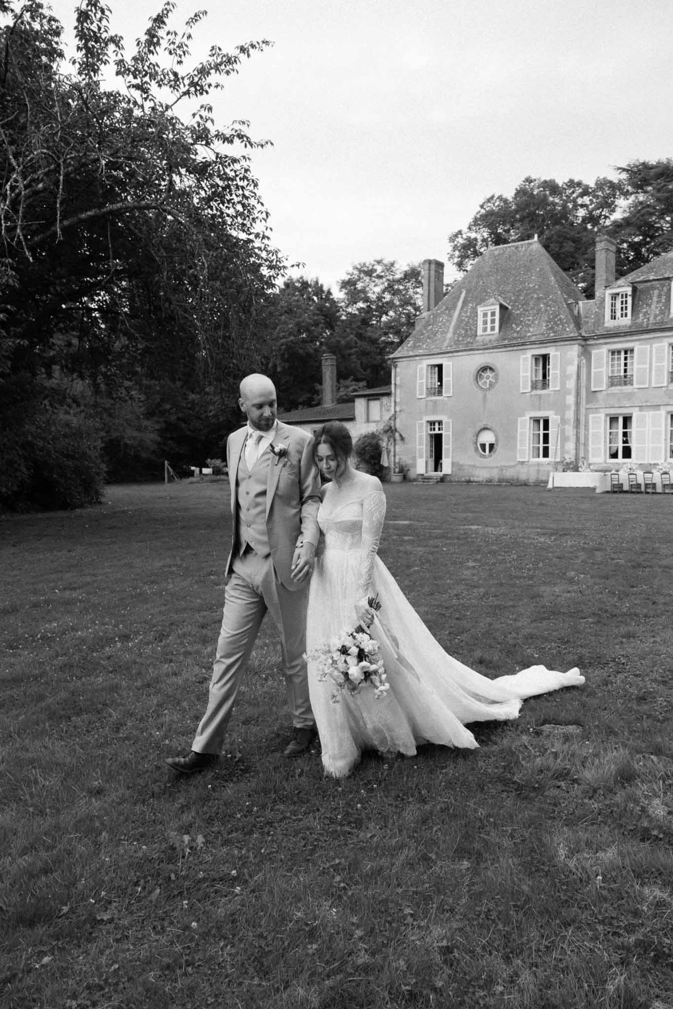 Wedding couple walking on château lawn in black and white portrait
