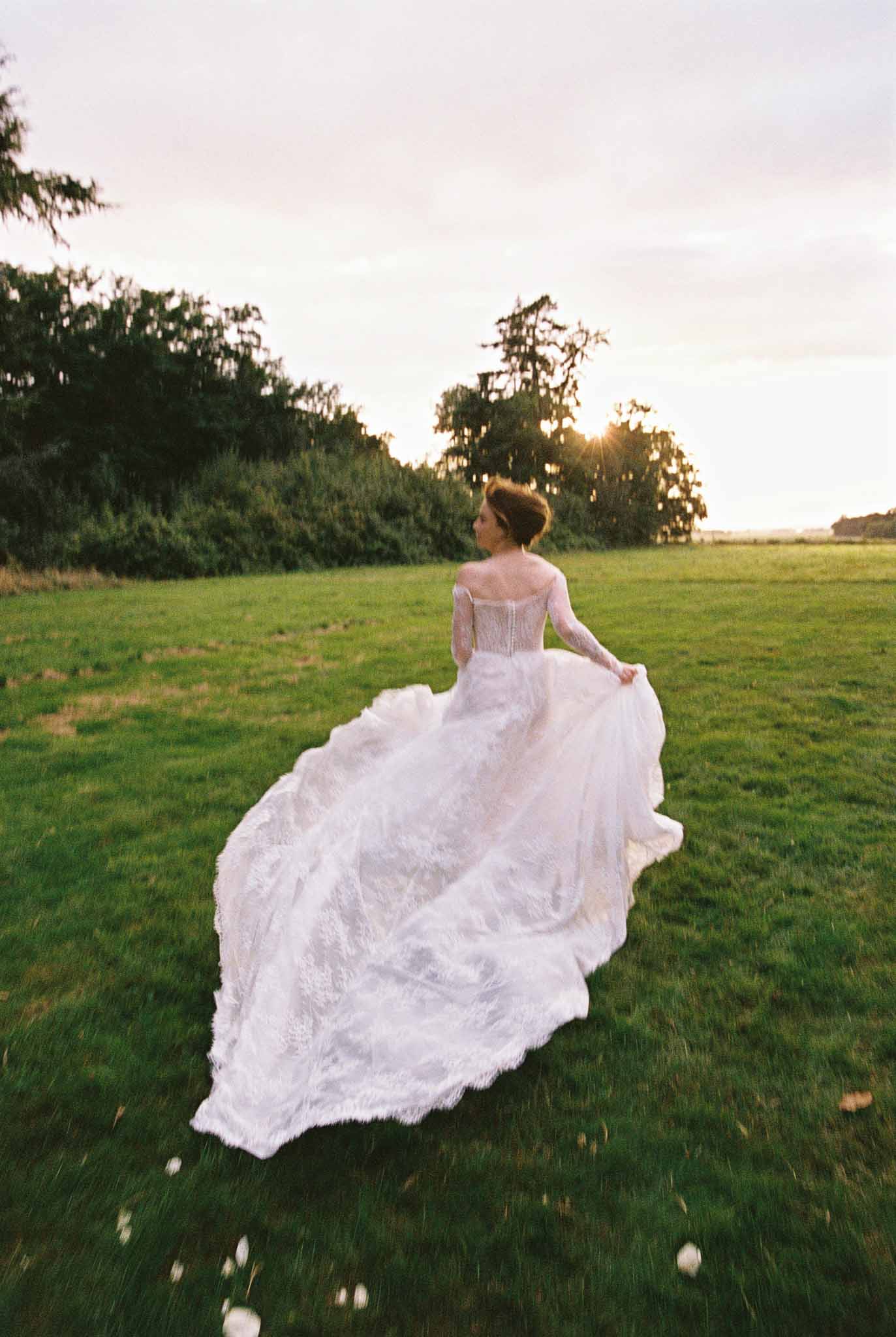 Bride in ivory wedding dress posing in countryside field during golden hour
