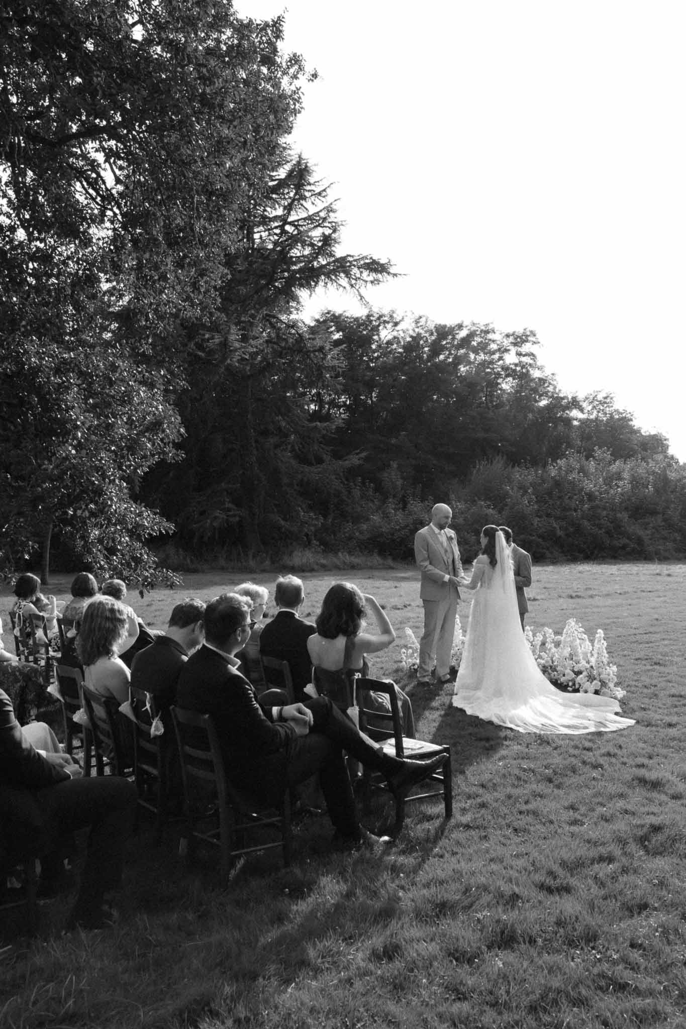 Outdoor wedding ceremony with bride and groom exchanging vows in open field with seated guests
