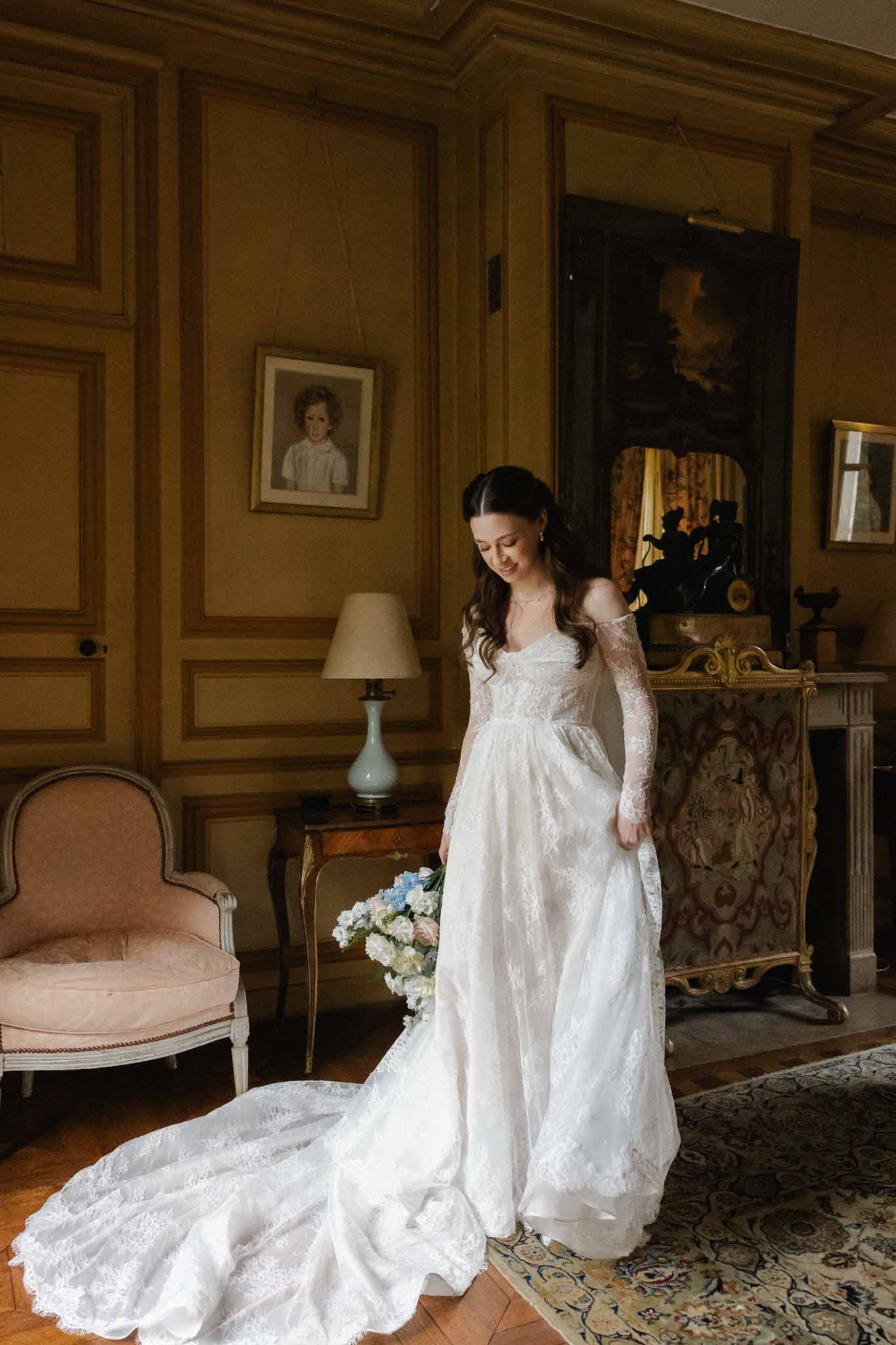 Bride in ivory lace wedding dress standing in ornate period room with classical furnishings