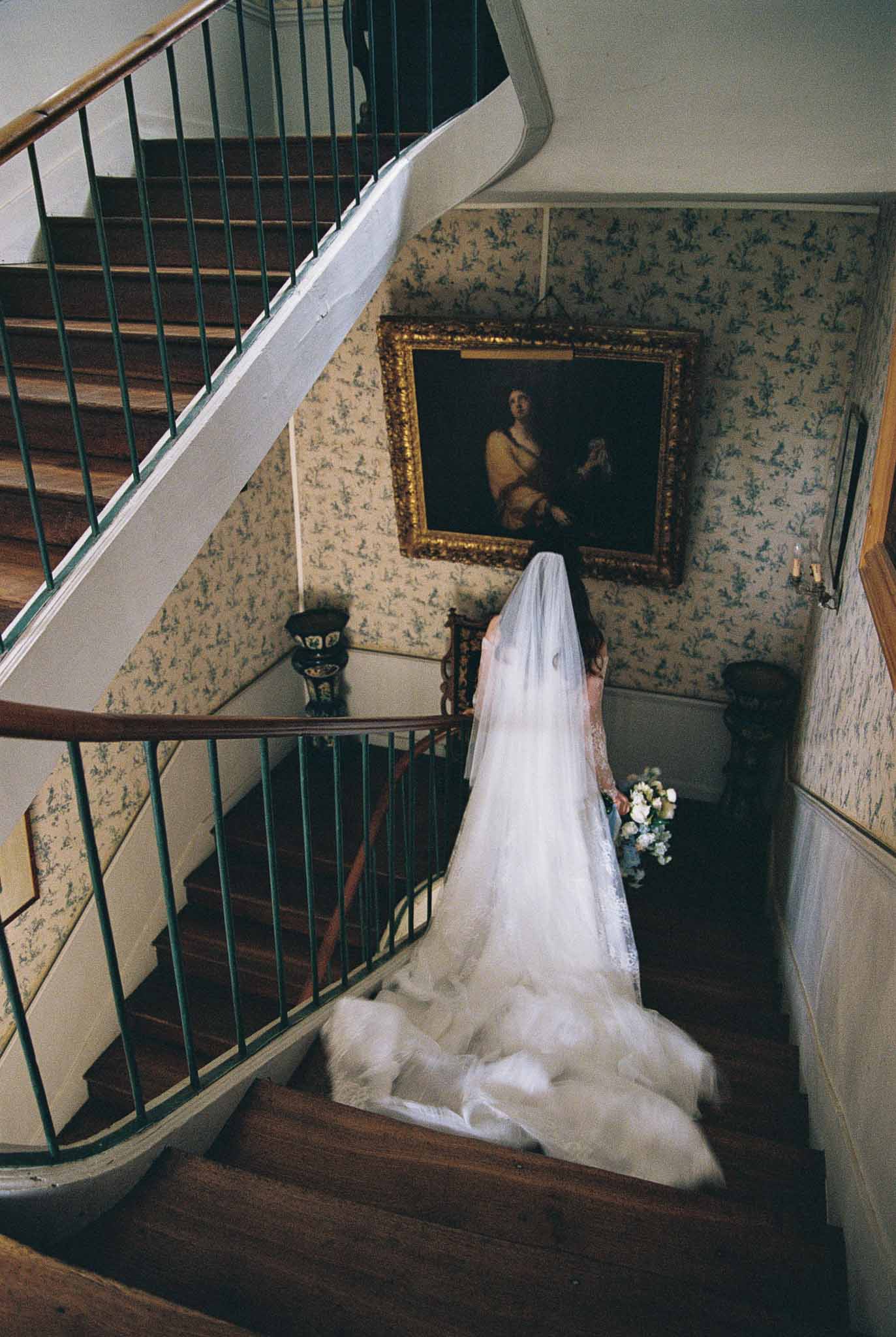 Bride descending curved staircase in historic interior with flowing train and veil