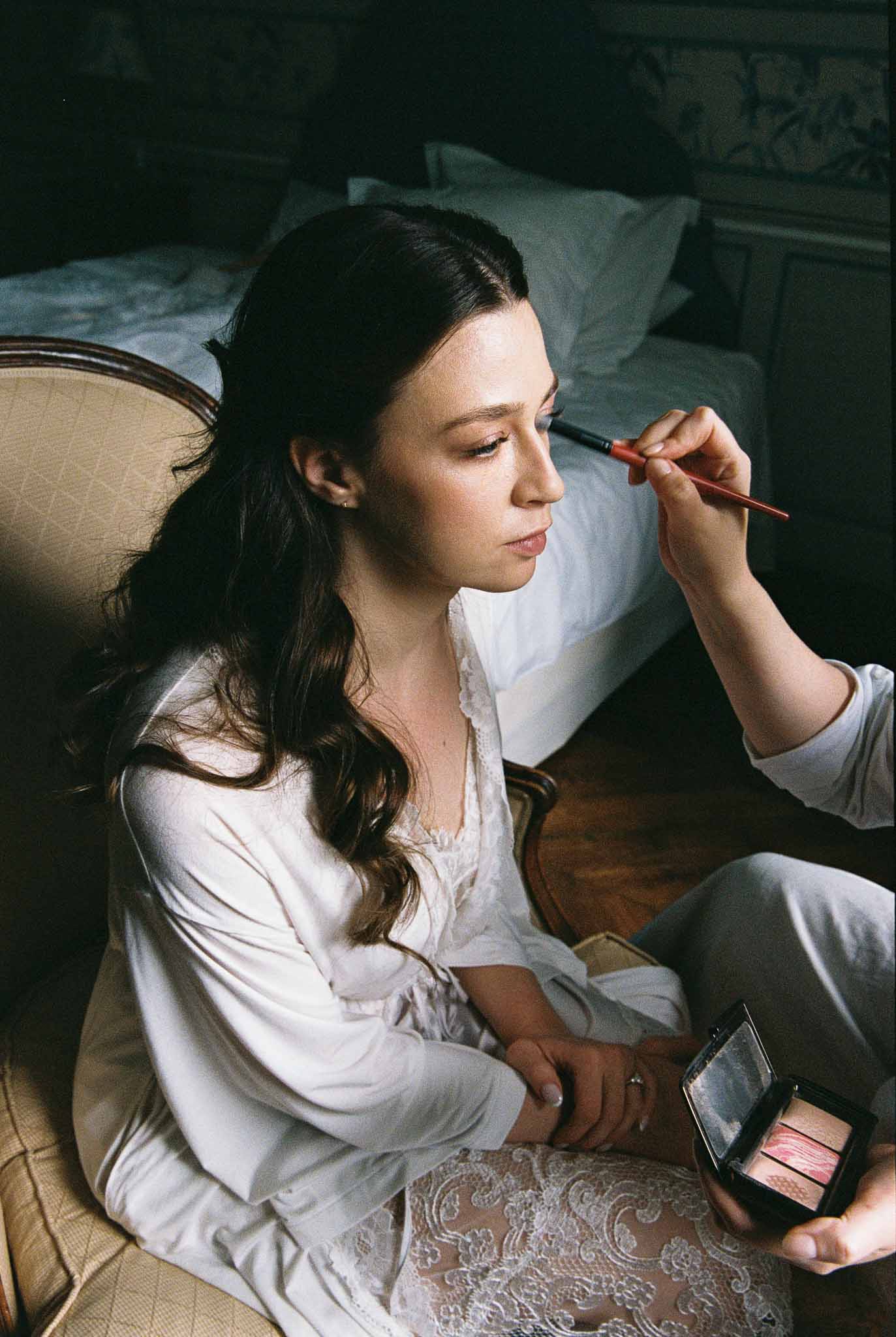 Bride applying makeup during getting ready preparations in bedroom