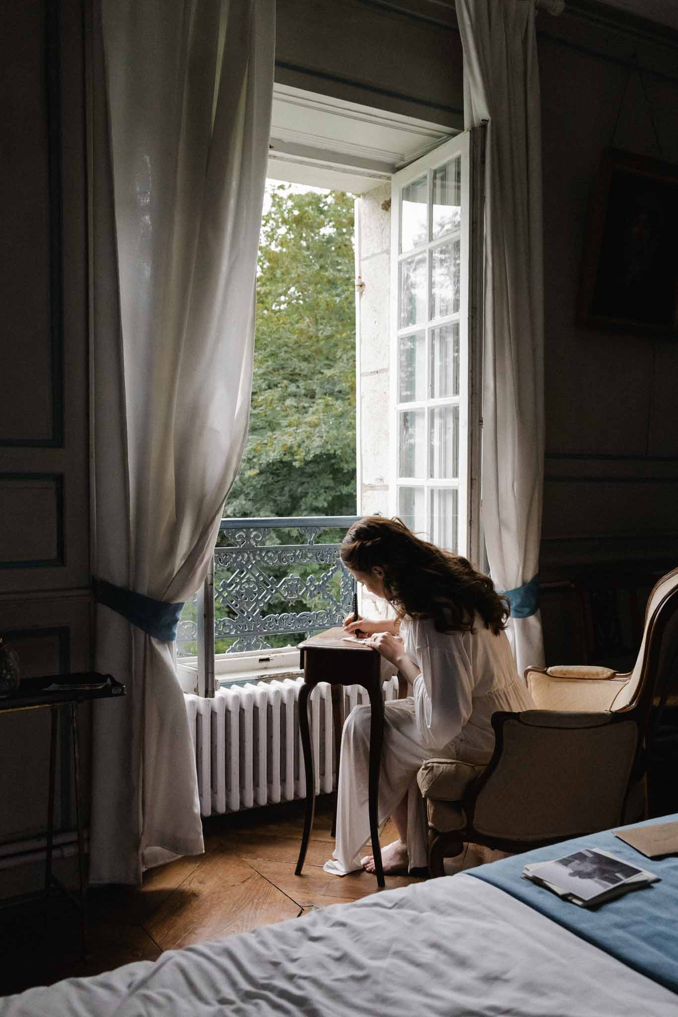 Bride writing at desk near French doors in historic château interior room