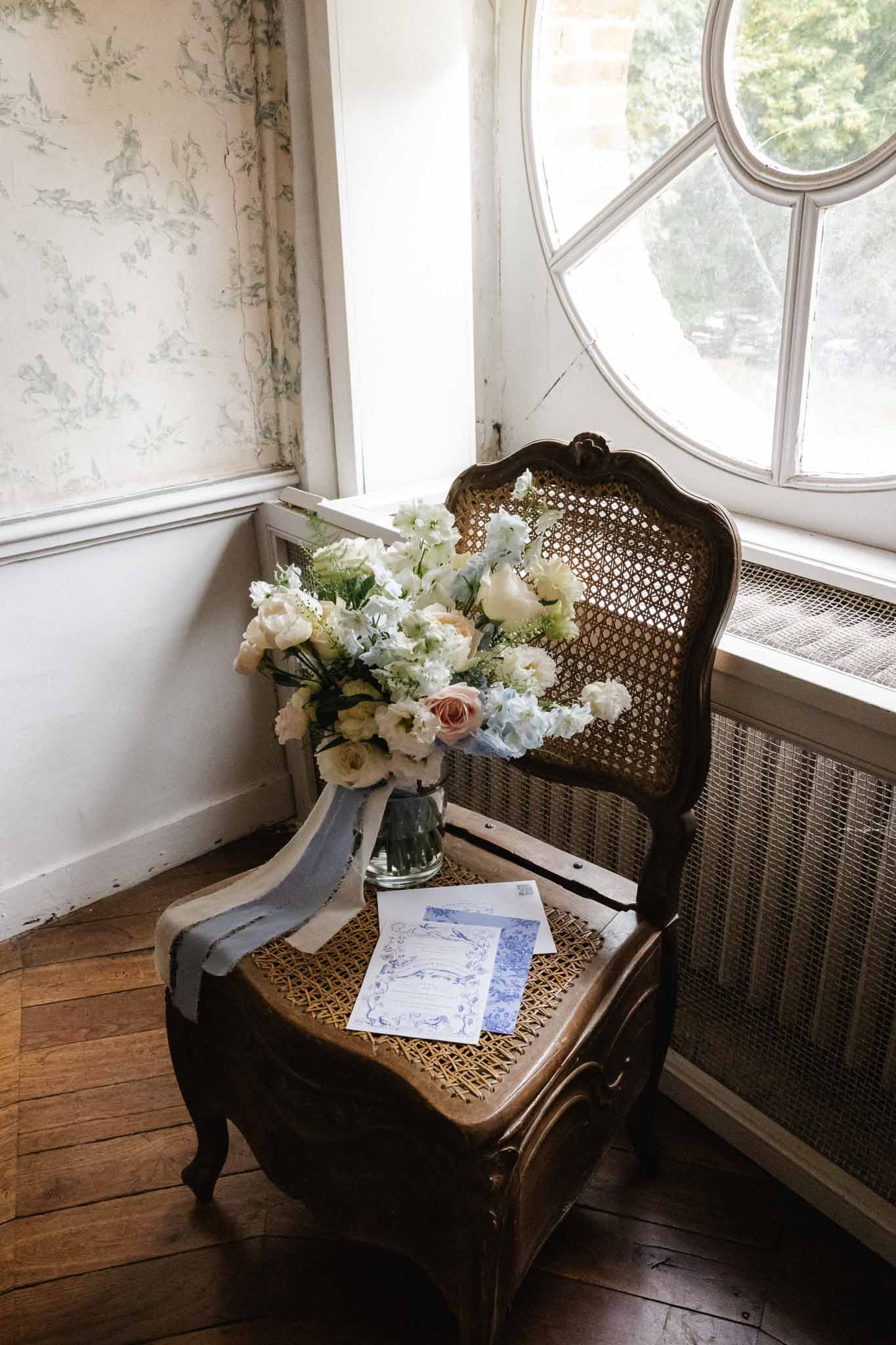 Bridal bouquet and wedding program arranged on vintage cane chair by period windows