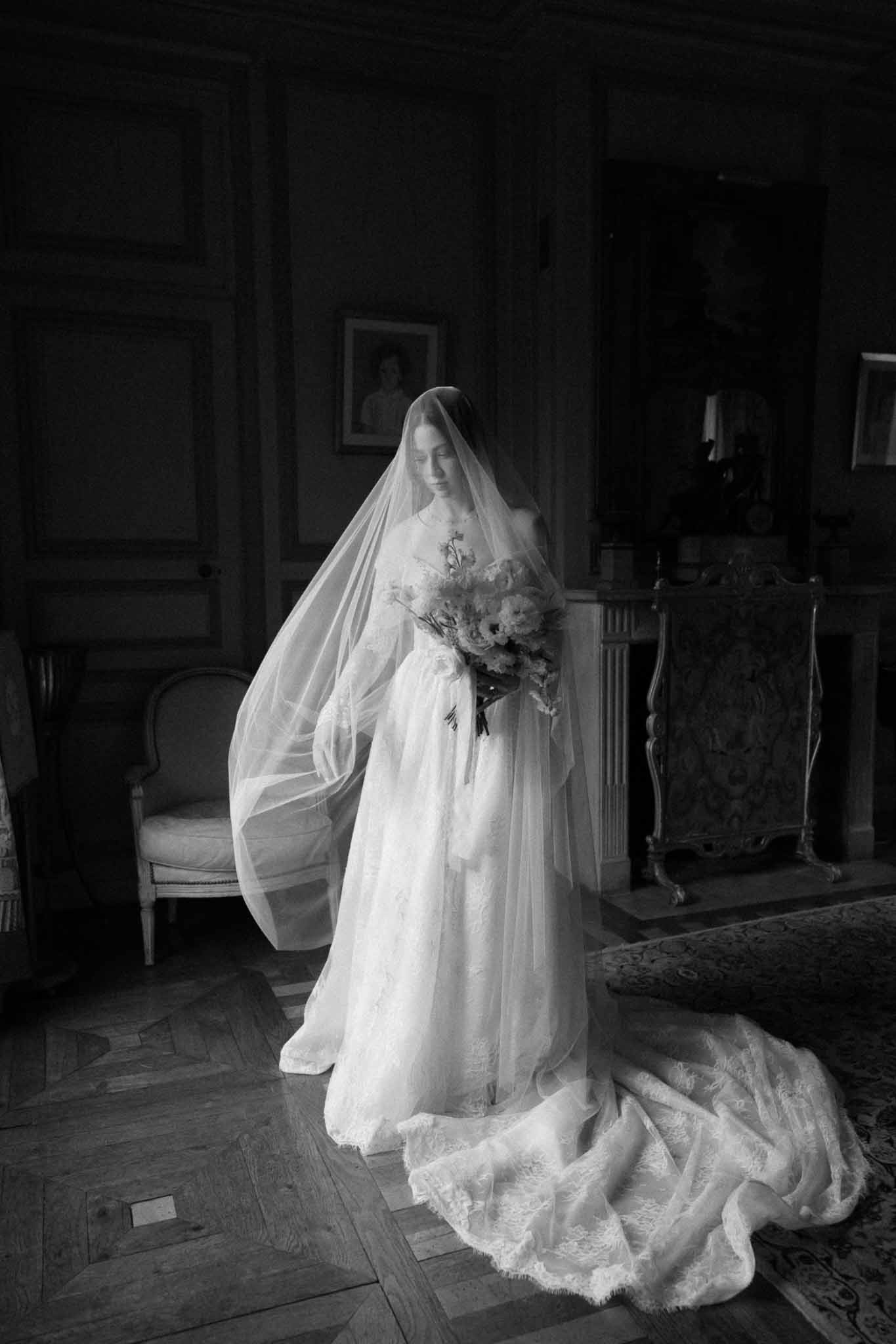 Bride in flowing gown with veil holding bouquet in formal salon interior