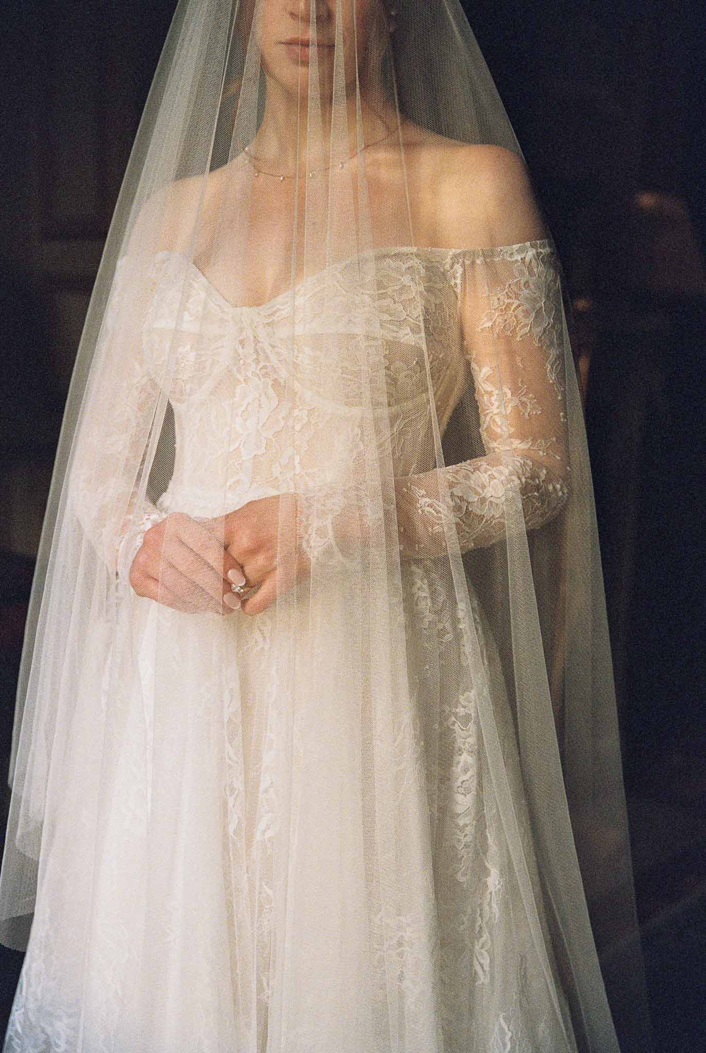 Bride in ivory lace wedding dress and full-length tulle veil against dark background