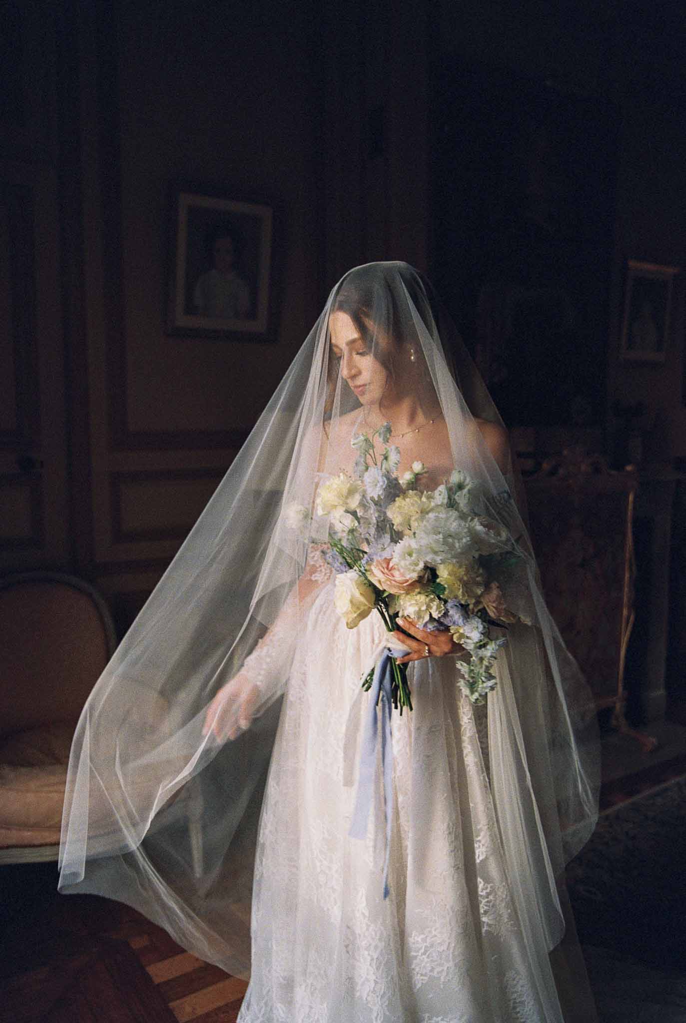 Bride in ivory lace dress and veil holding bouquet in chapel interior